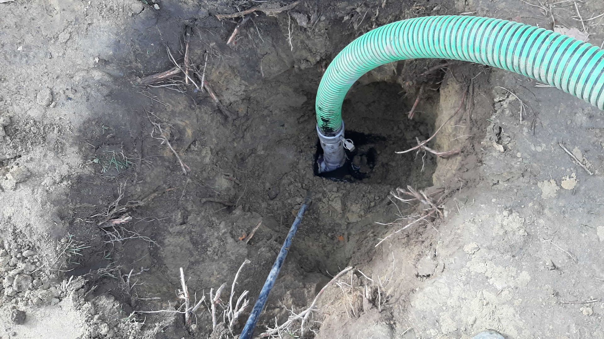 Green hose entering a dark hole in the ground; soil and roots visible.