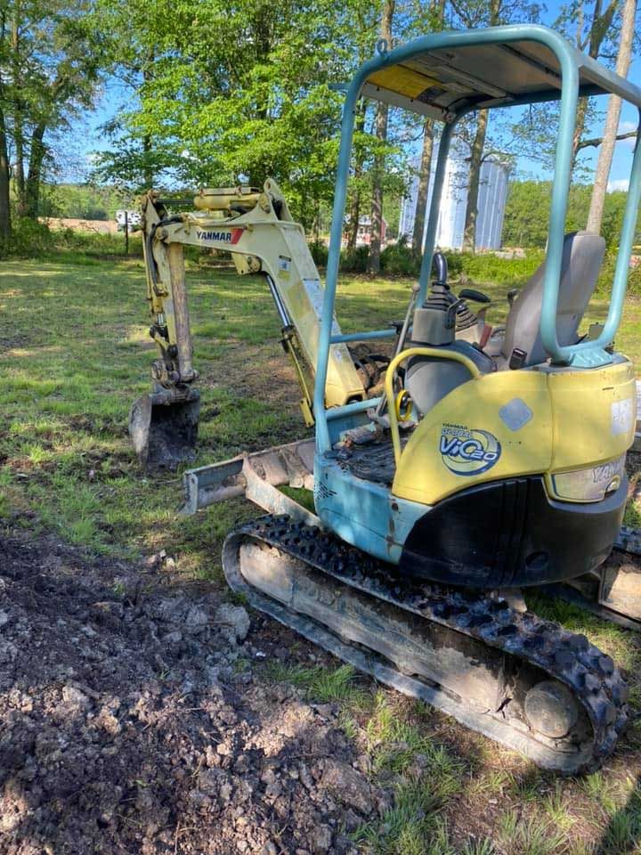 Small yellow and blue excavator digging in a grassy field.