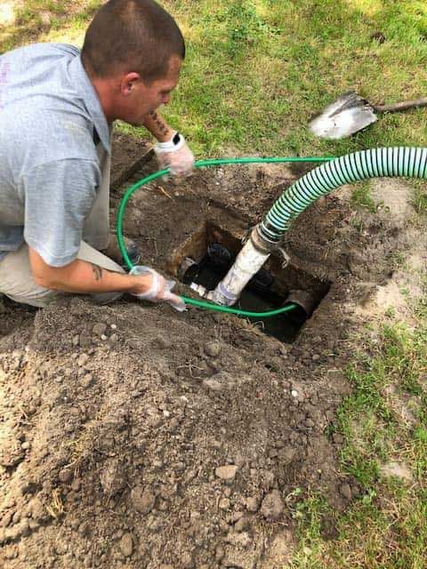Man using a hose to pump a septic tank in a grassy yard.