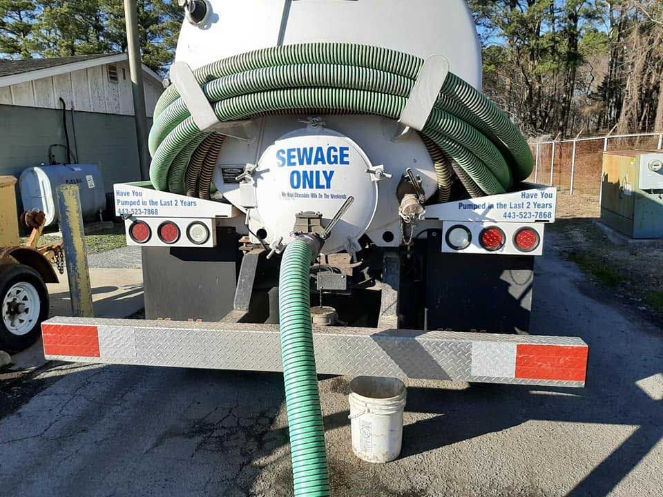 Rear view of a sewage truck with a hose connected, parked in a yard. 