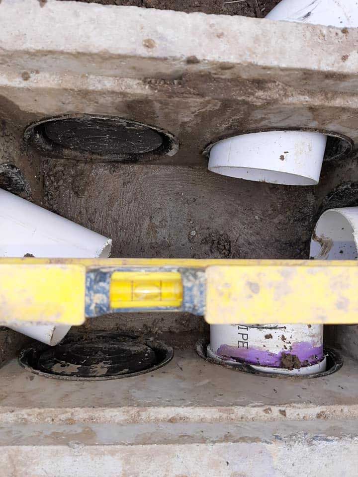 A level resting on concrete with PVC pipes, inside a grey concrete structure.