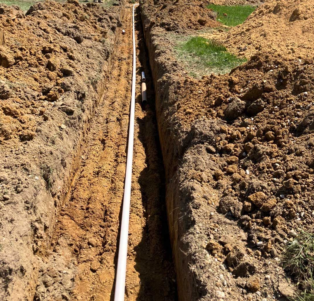 A trench in brown soil with a white pipe running through the center.
