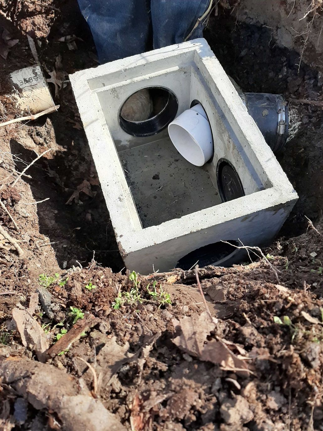 Concrete drainage box with pipes in a dirt trench.