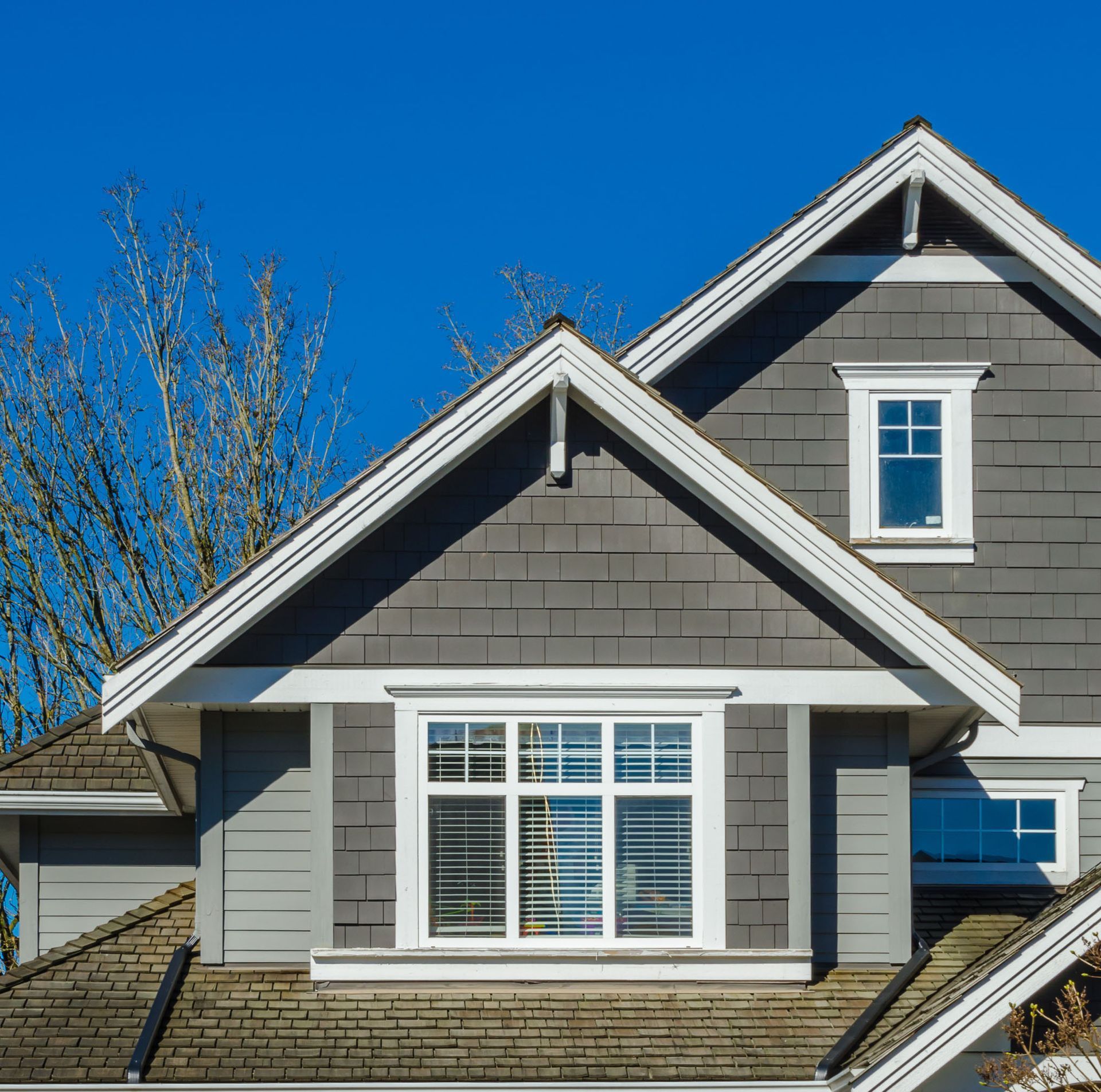 Gray house exterior with white trim and multiple gables against a bright blue sky