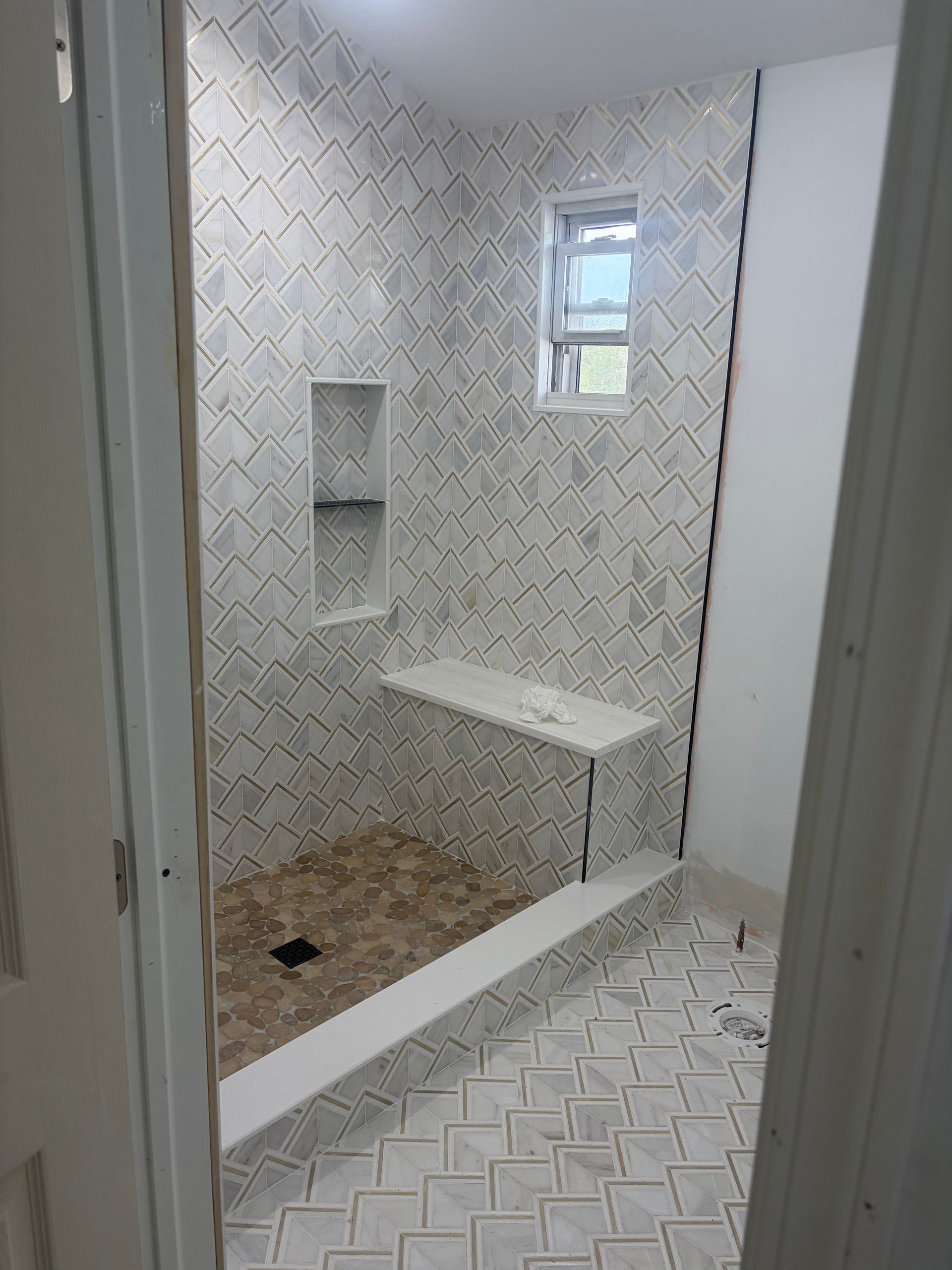 Tiled shower room with built-in shelf, bench, and window, showing two different floor tile patterns.