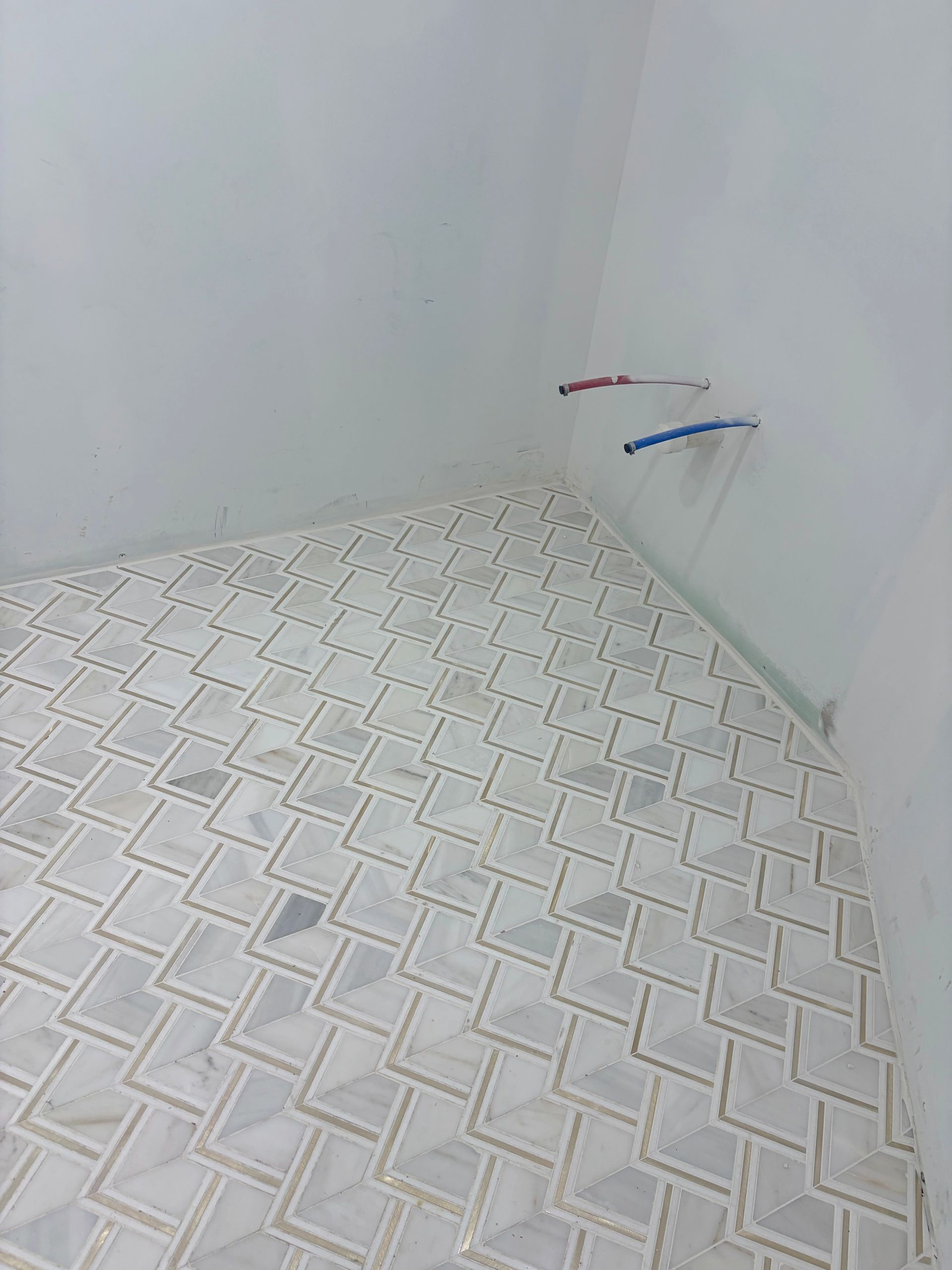 Empty tiled room corner with wall plumbing pipes protruding from the wall