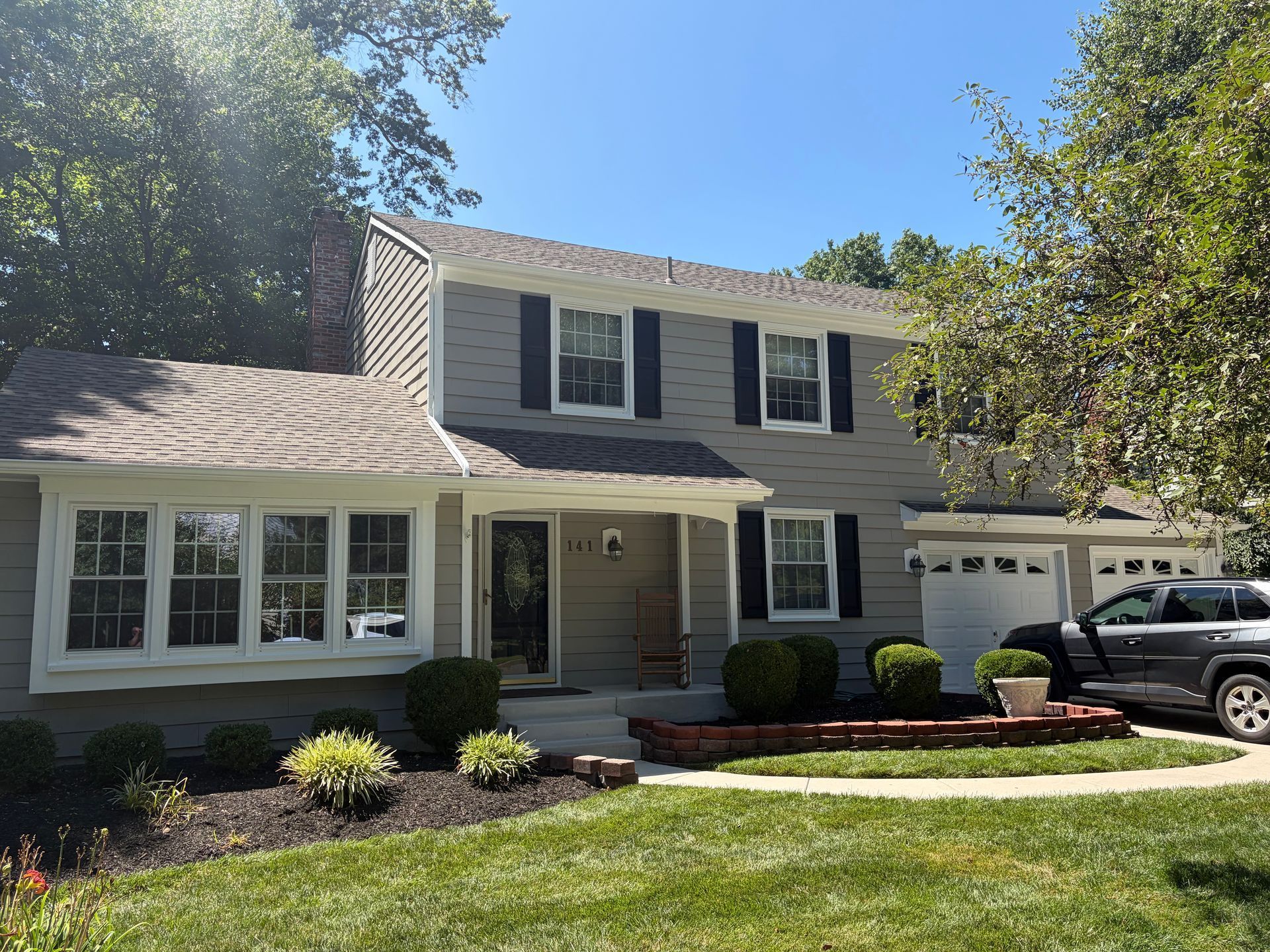Two-story white house with black shutters, front porch, and attached garage under a sunny blue sky