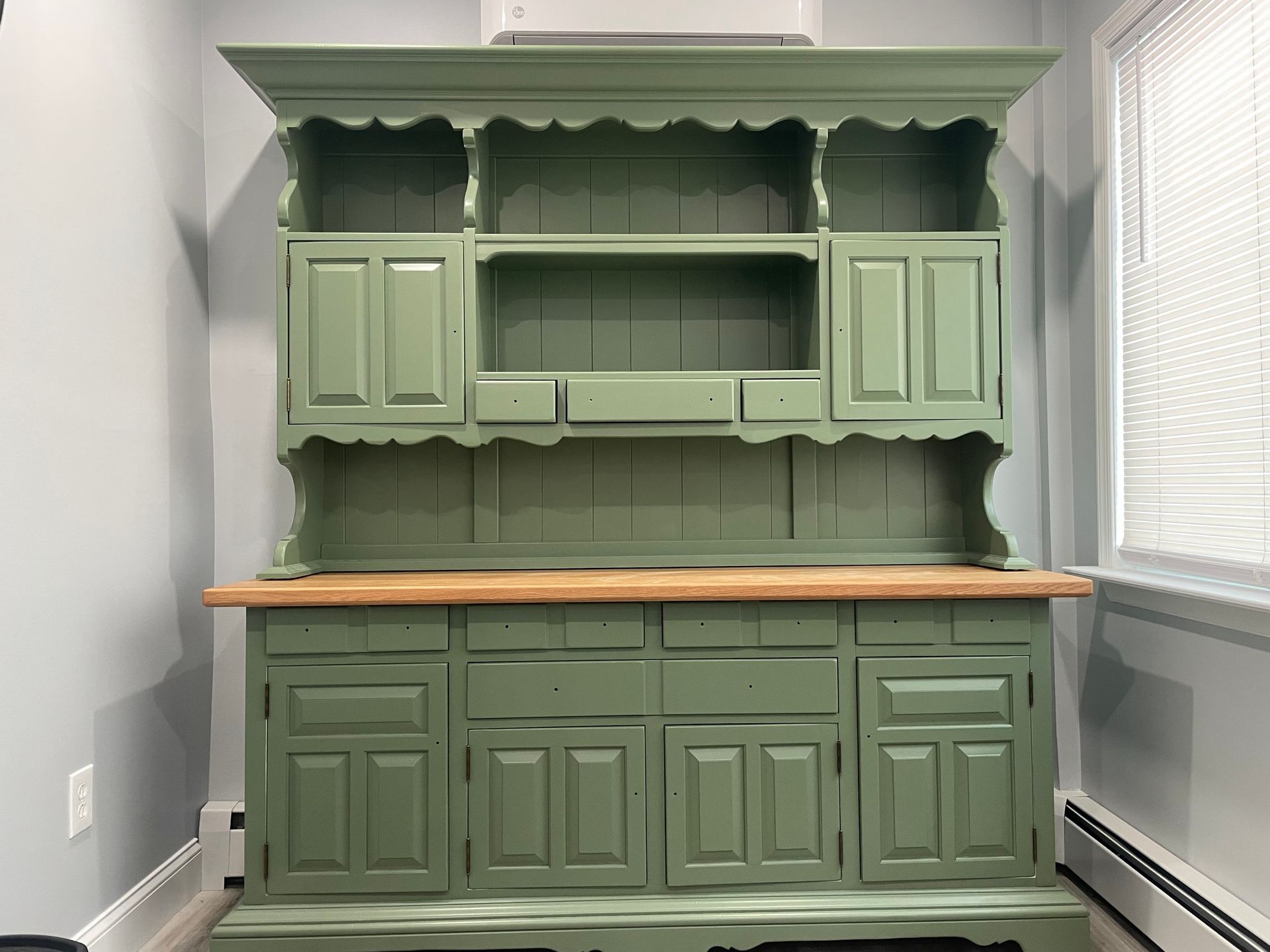 Green vintage hutch with wooden countertop against a white wall in a bright room