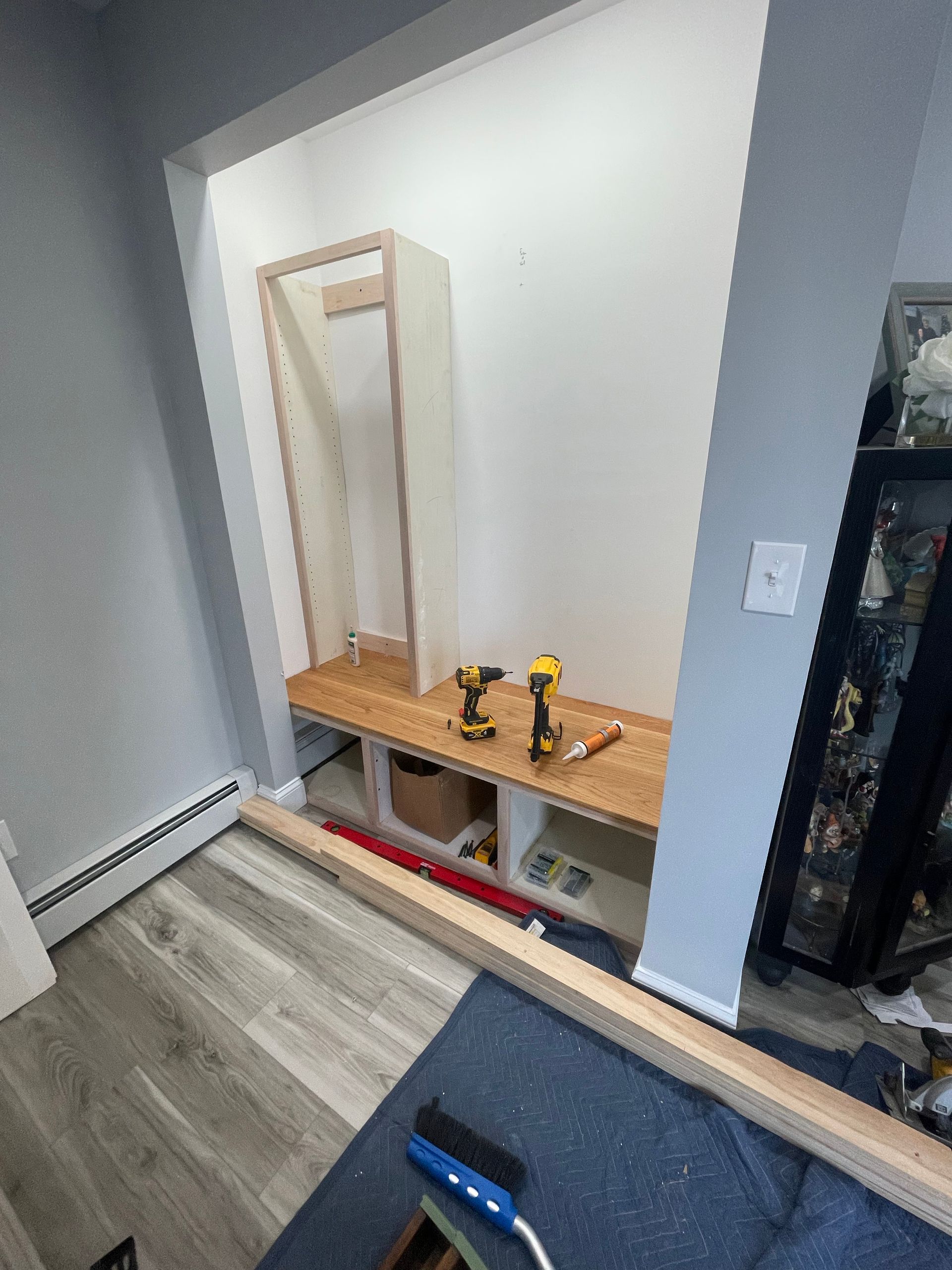Closet nook with a wooden bench, mirror, tools, and a red level on the floor.