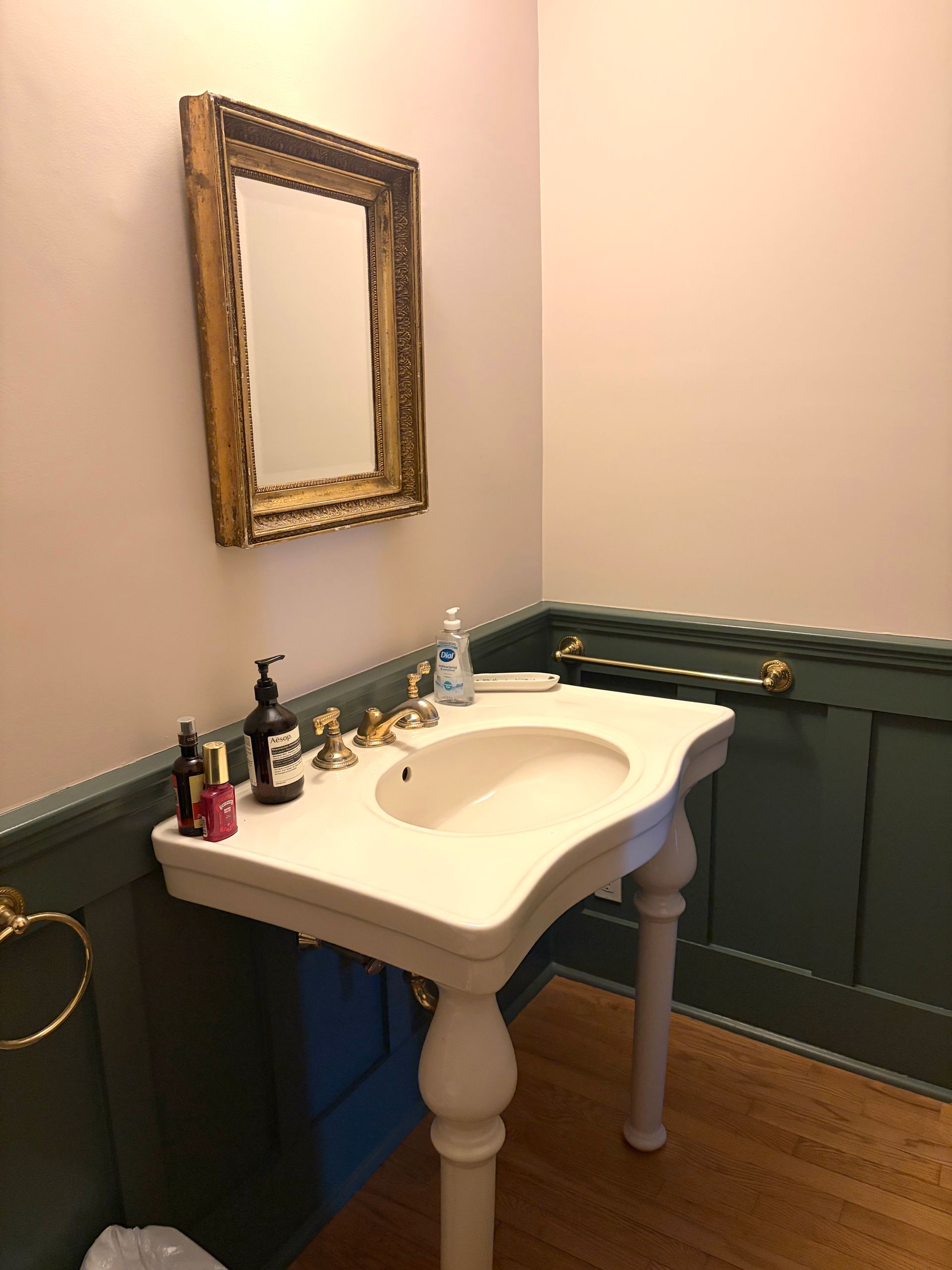 Small bathroom vanity with white sink, ornate mirror, and green wainscoting.
