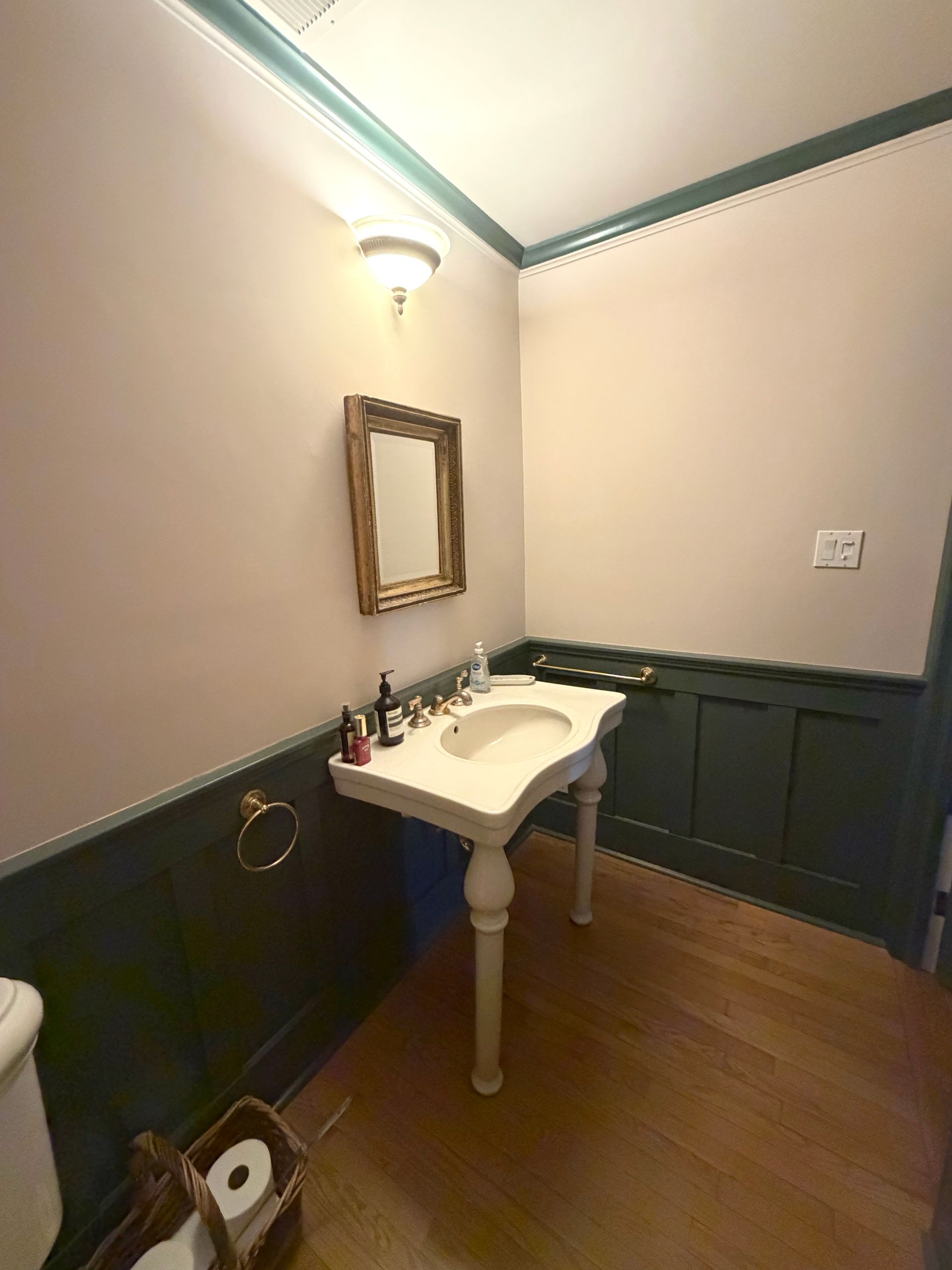 Small bathroom with dark wainscoting, white pedestal sink, mirror, and wood floor.