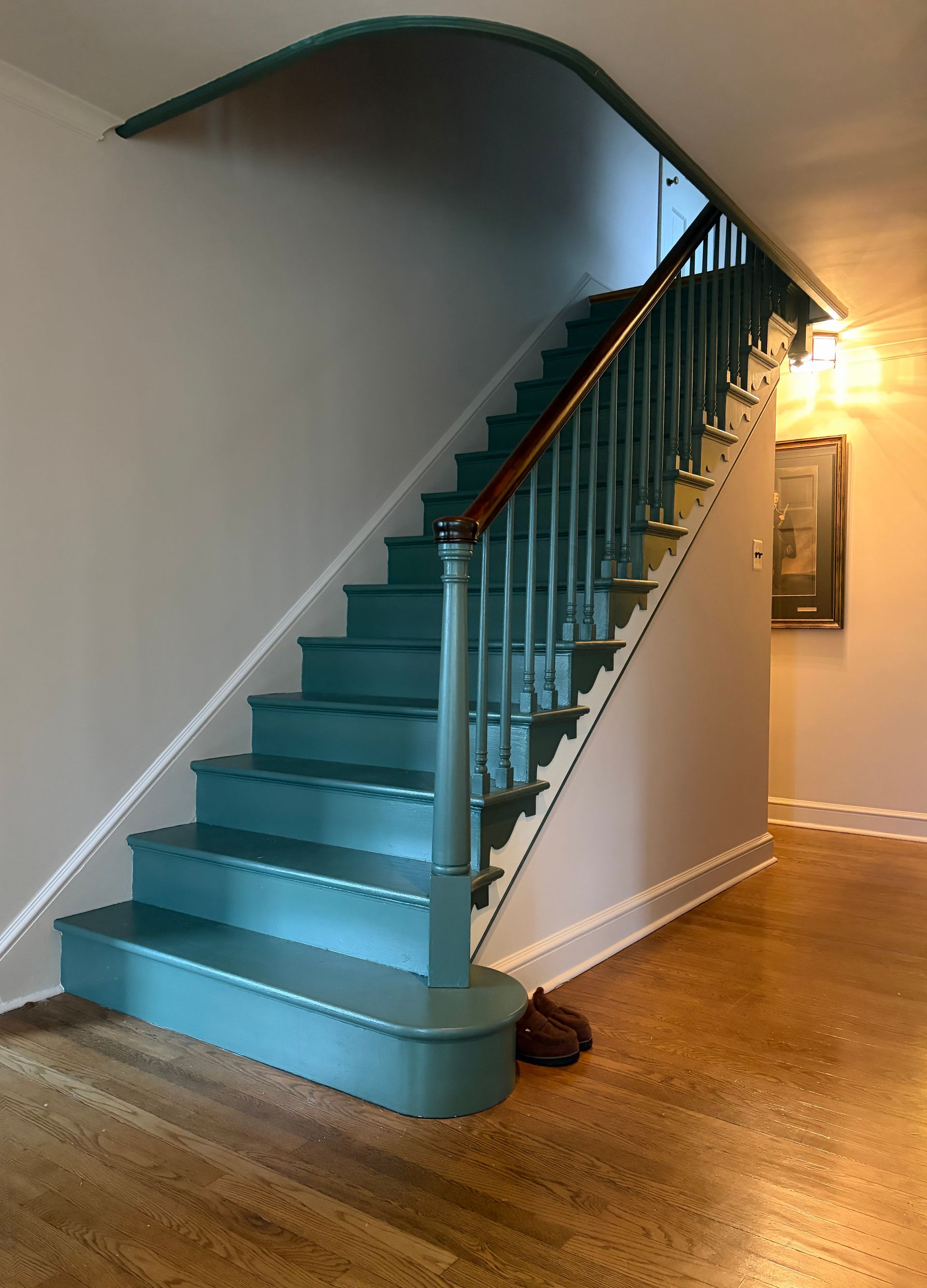 Teal staircase with curved railing in a hallway, leading up from a wood floor.