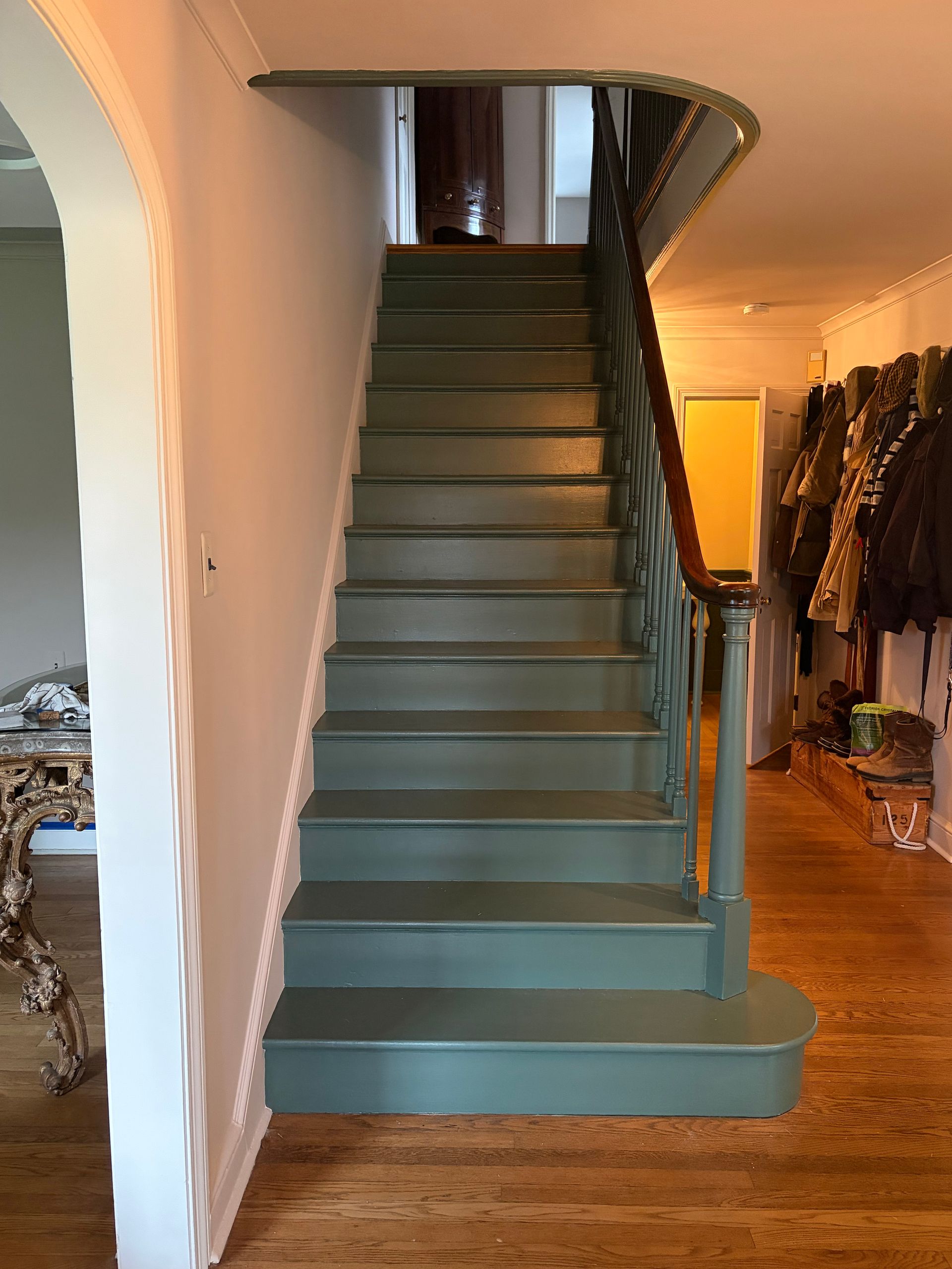 Teal staircase in a hallway with wood floors and coat rack on the right