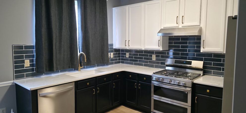 Compact kitchen with white cabinets, black tile backsplash, dark curtains, and stainless steel stove and sink