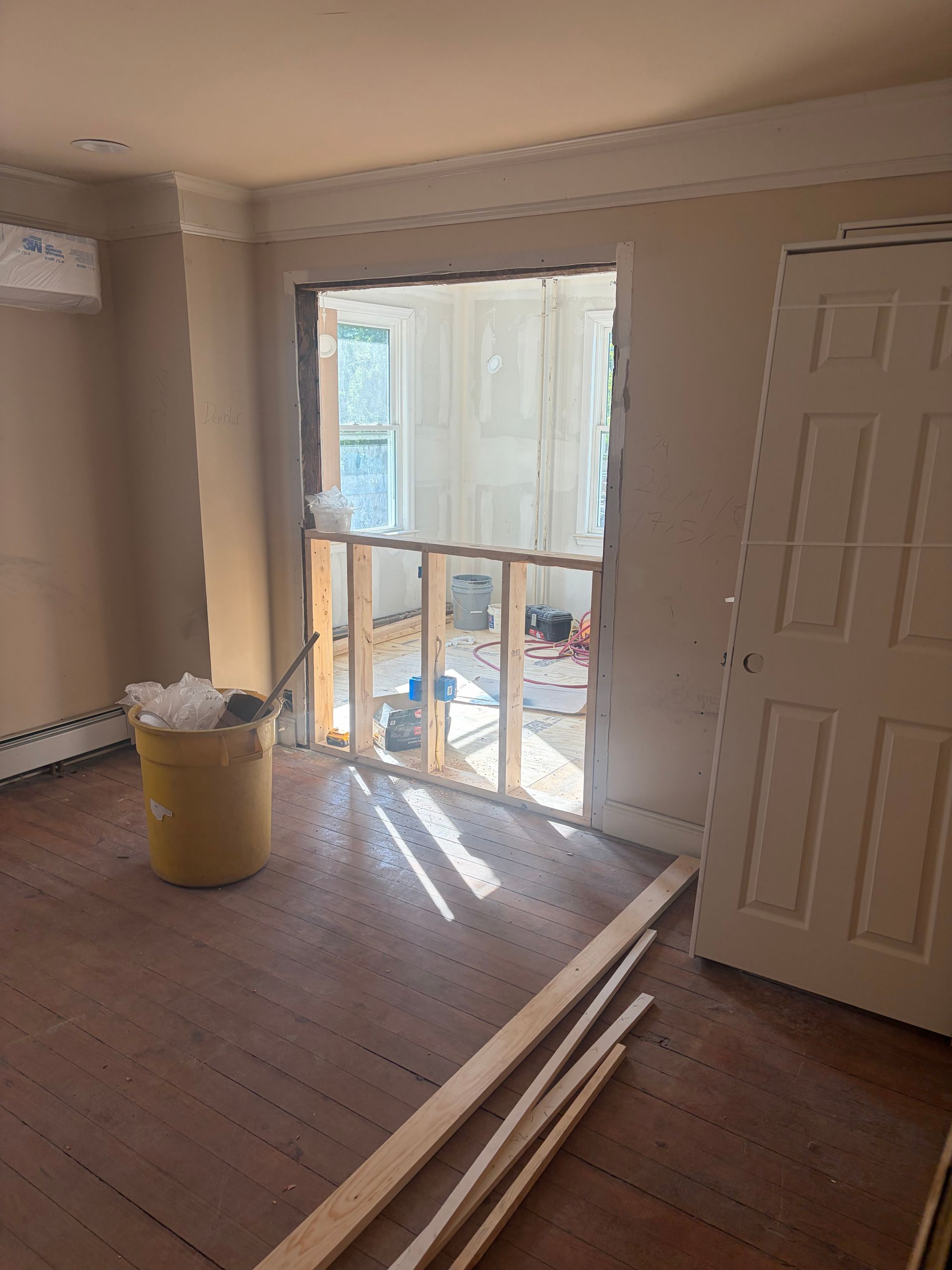 Partially renovated room with exposed wall framing, open door, broom, and construction materials on floor