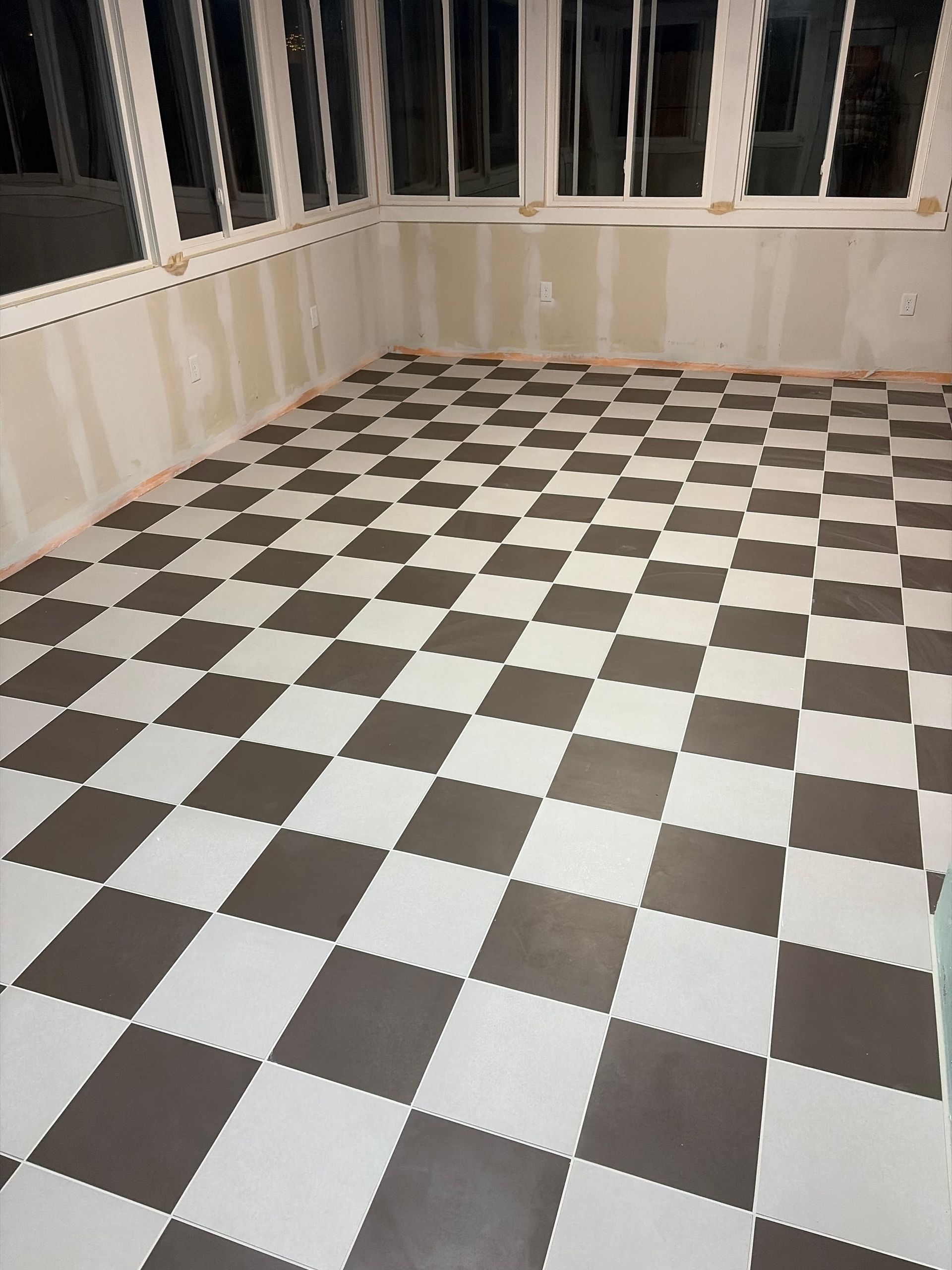 Empty room with black-and-white checkered tile floor and large windows along the walls