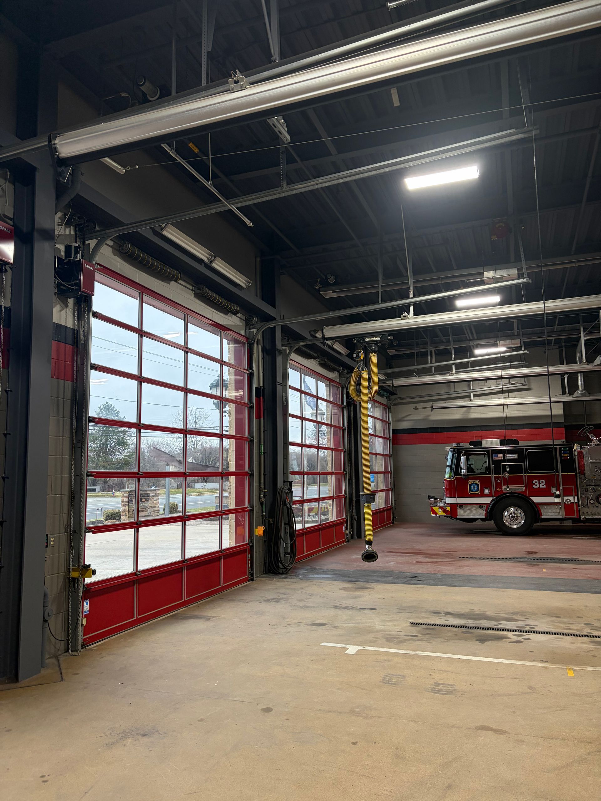 Fire station interior with open red garage doors, concrete floor, and a red fire truck parked inside