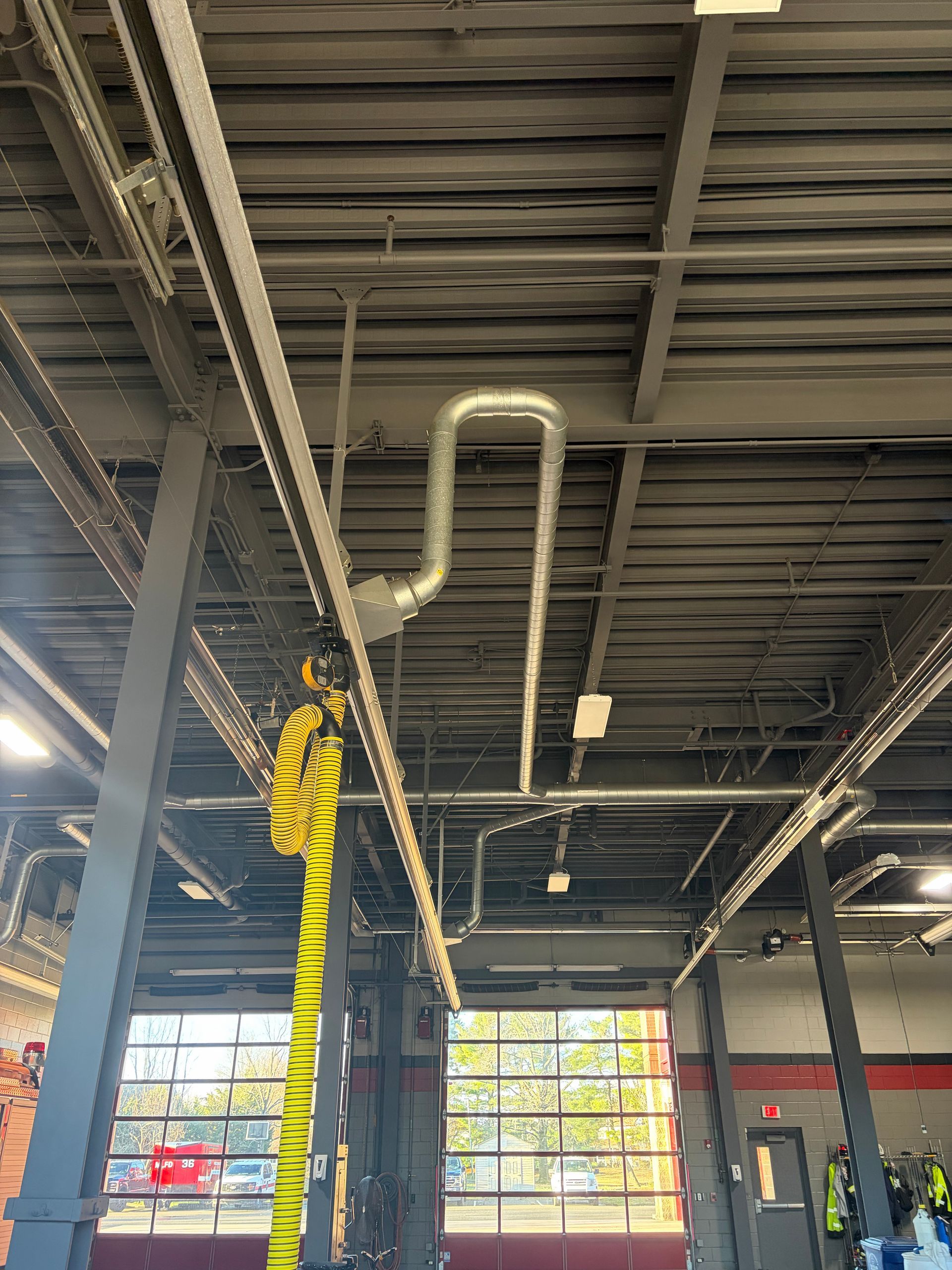 Industrial interior with exposed ceiling pipes, steel beams, and large windows lit by daylight