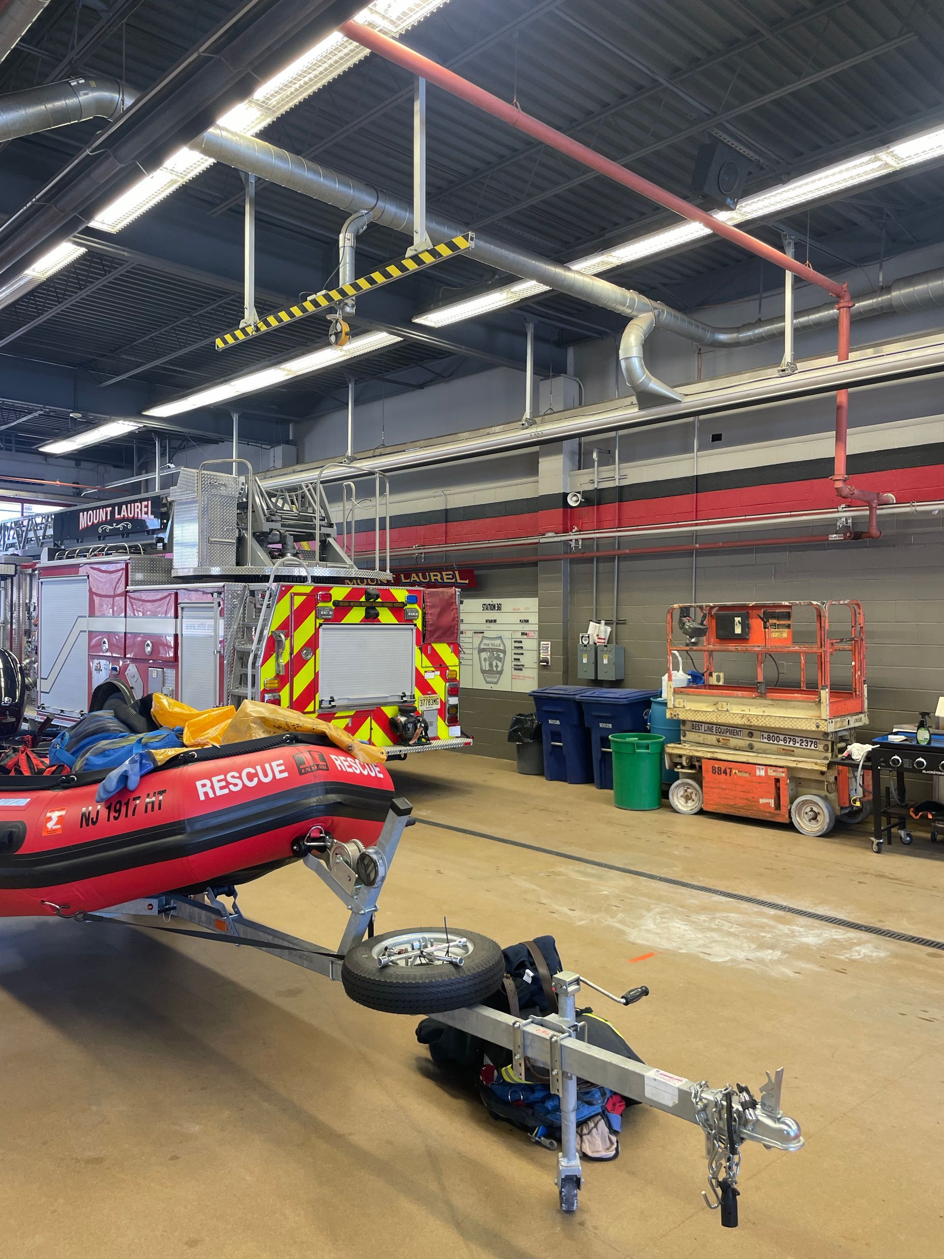 Emergency vehicles and rescue equipment inside a station garage with overhead piping and open floor area