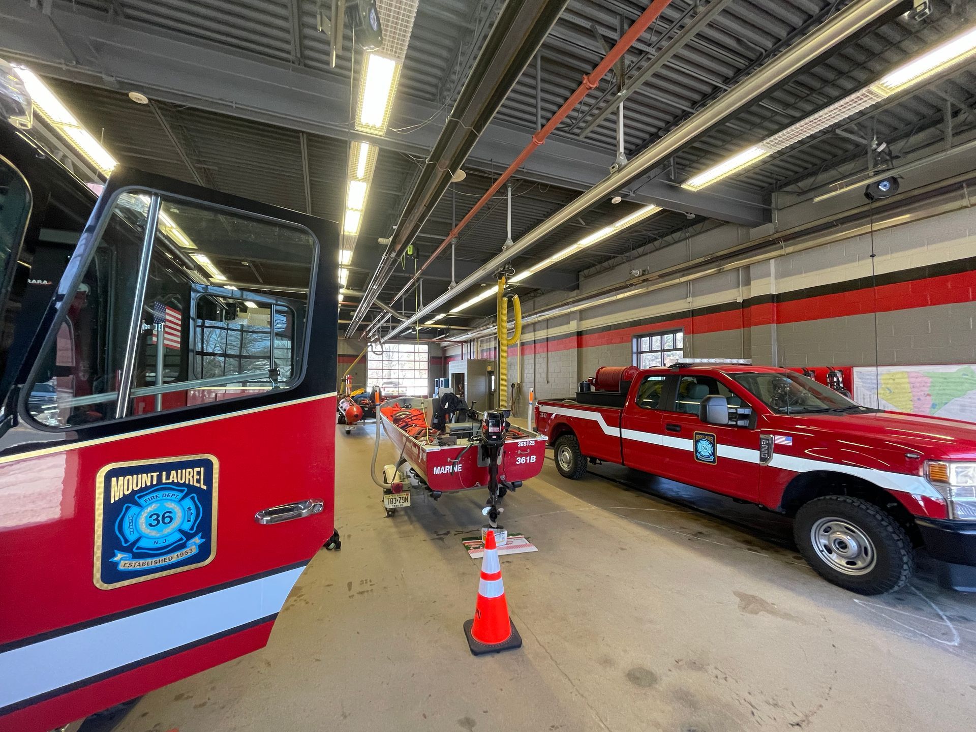 Two red fire trucks parked inside a fire station bay with orange cones and equipment inside.