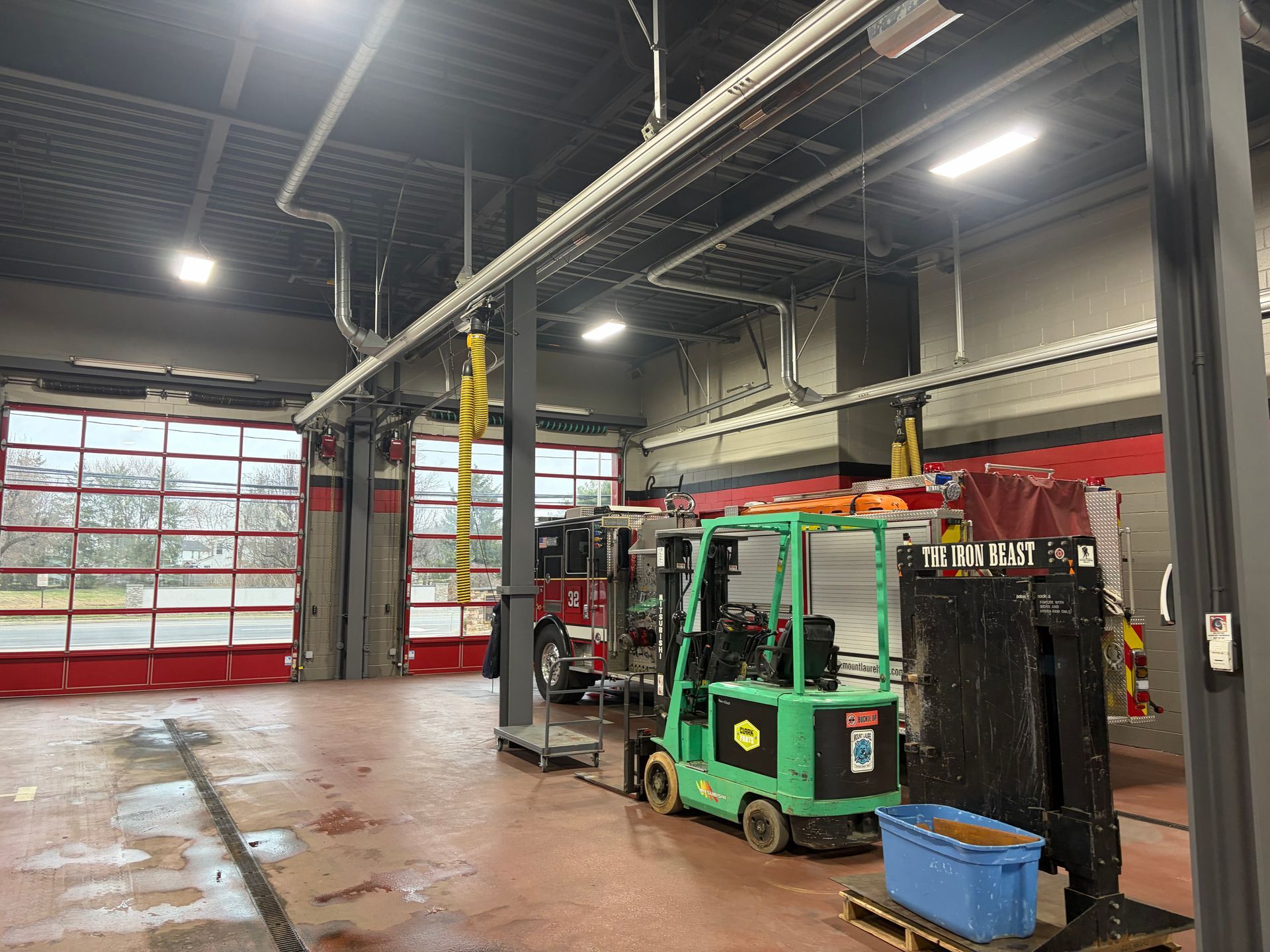 Green forklift in an industrial garage with open red bay doors and wet concrete floor.