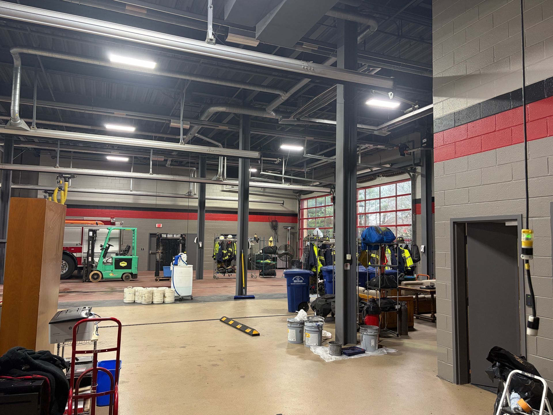 Industrial garage interior with concrete floor, metal beams, equipment, and red-striped walls