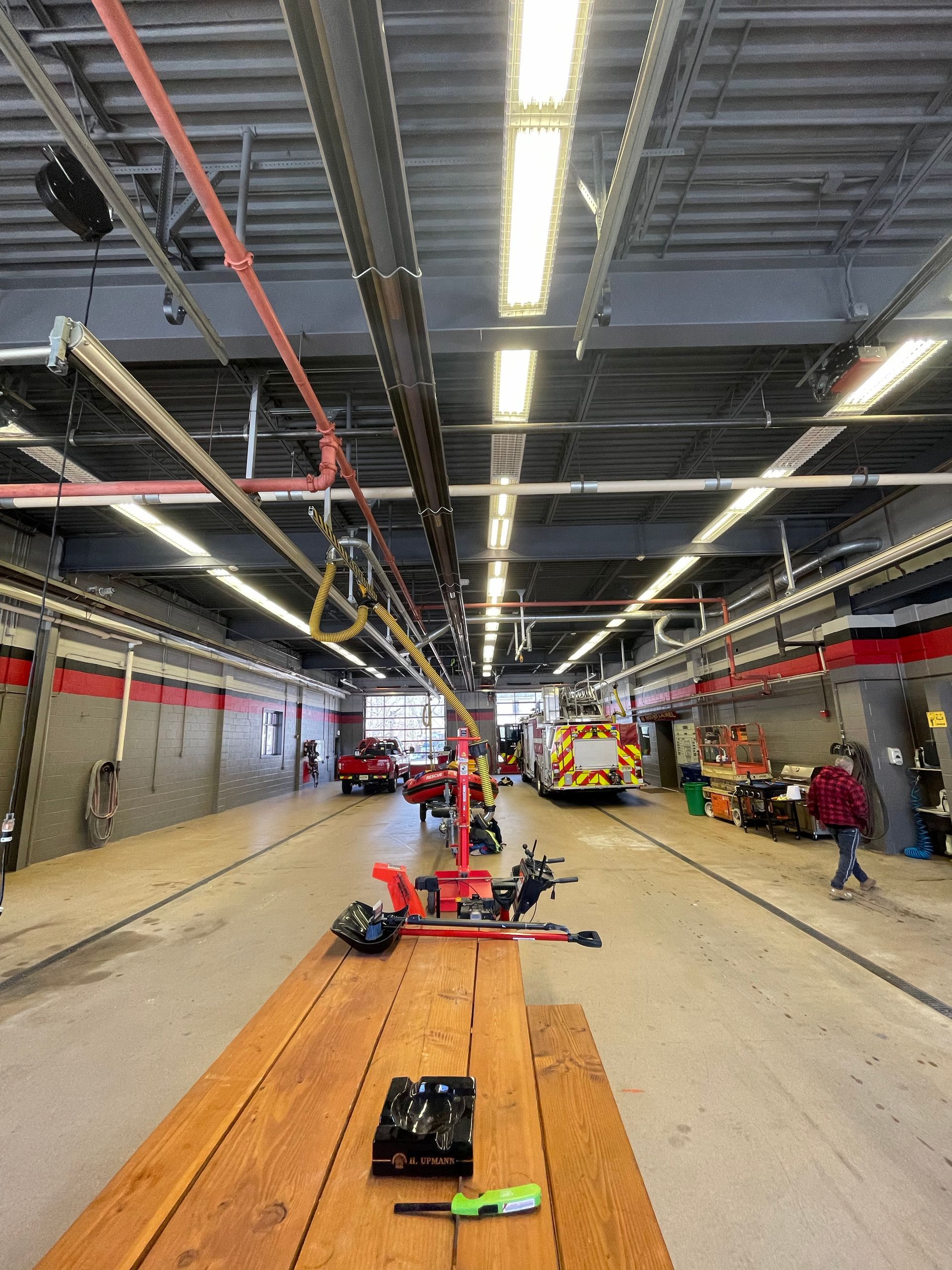 Wide garage-like indoor work area with a long central table, tools, and people working on vehicles.