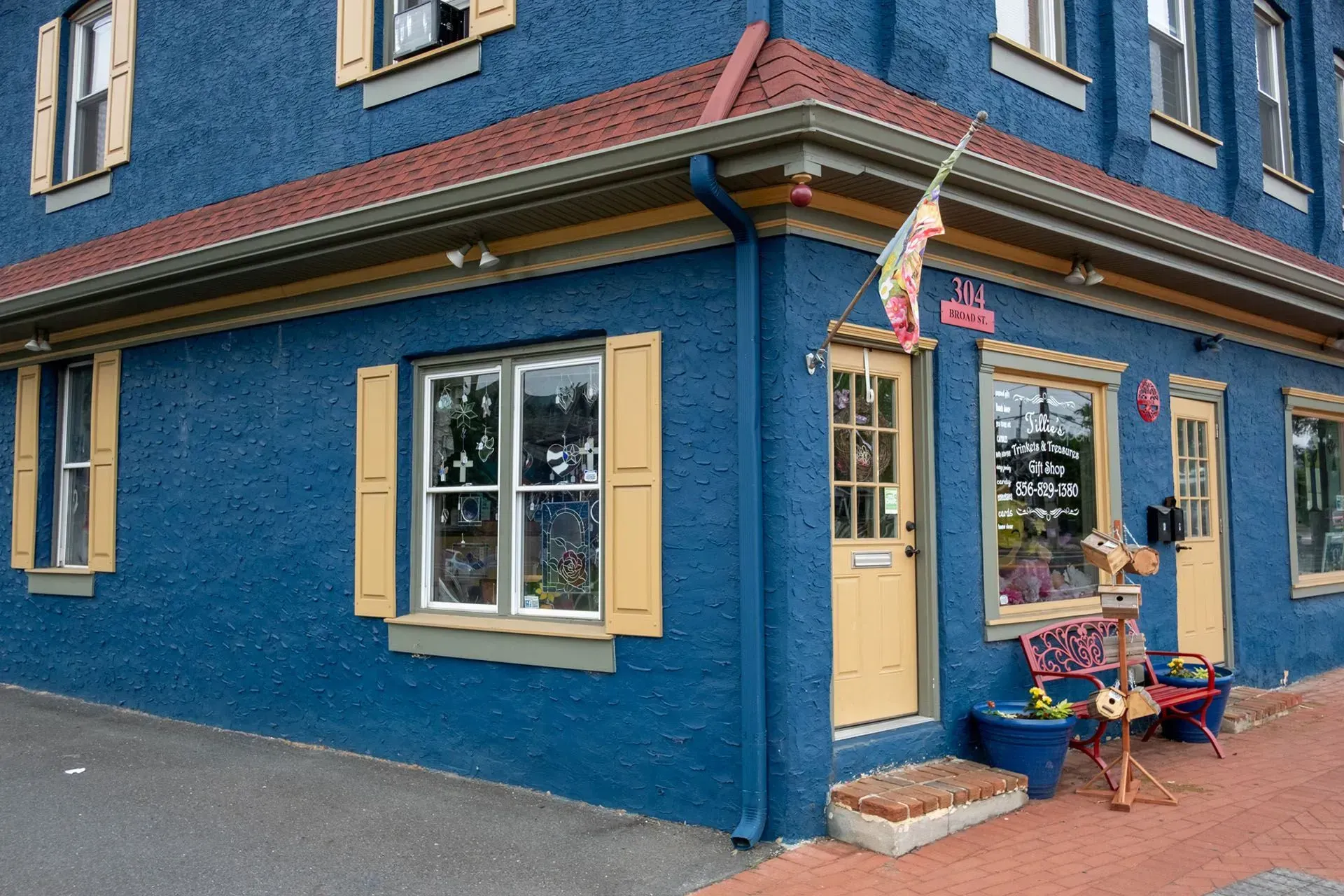 Blue building with yellow trim and doors, red roof. Shop with decorative items displayed.