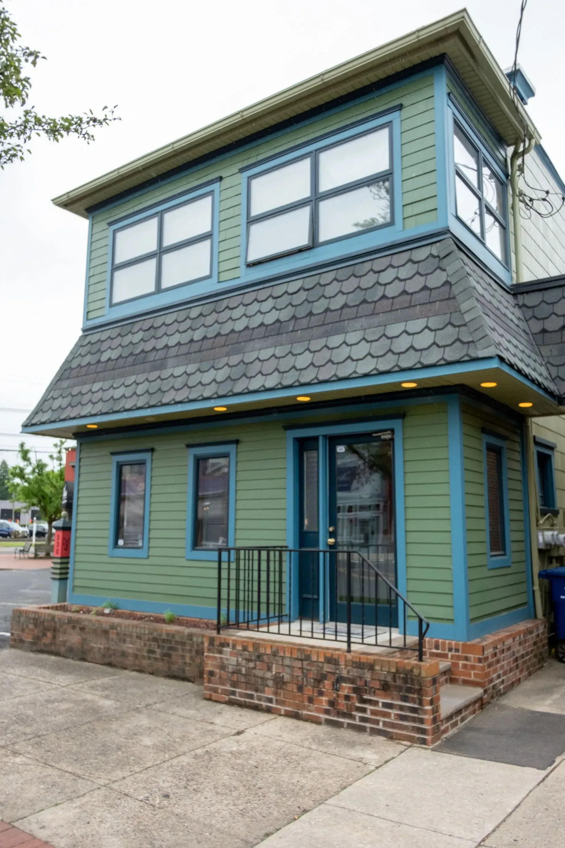 Two-story teal and blue building with angled roof and windows; brick base and railing.