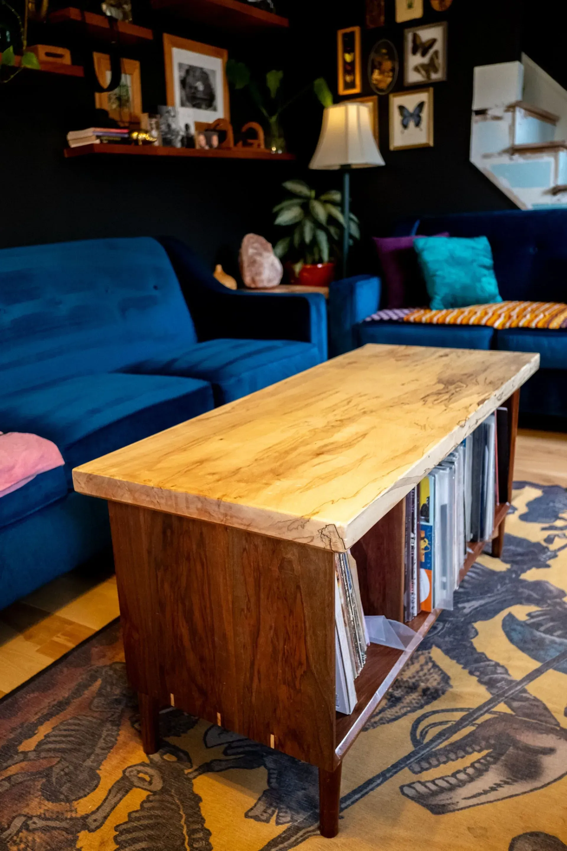 Wooden coffee table with magazine storage, in a living room with blue sofas and a rug.