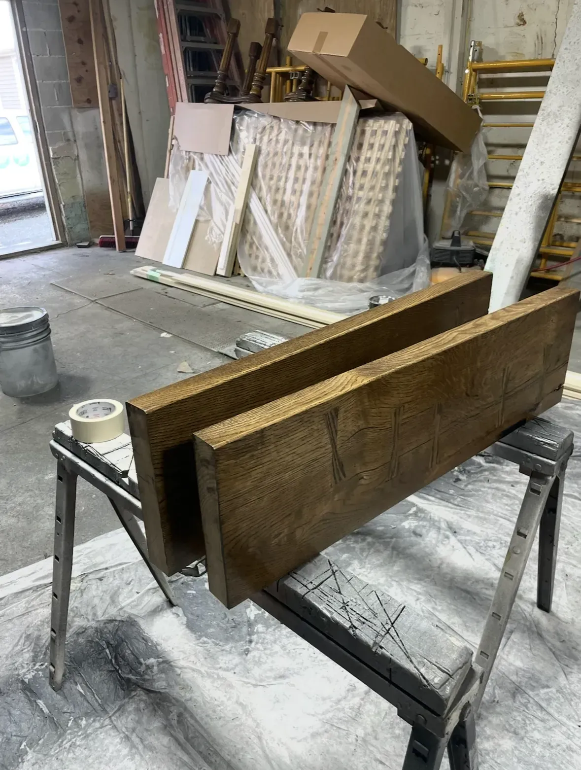Two stained wooden planks on sawhorses in a workshop setting.