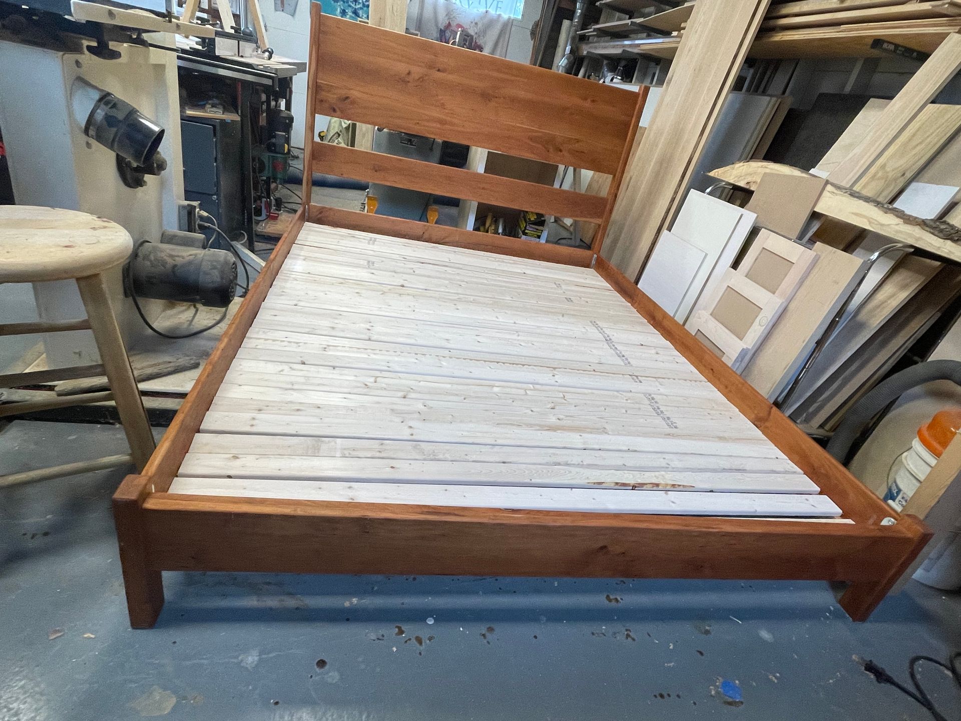 Wooden bed frame in workshop, with headboard and slats.
