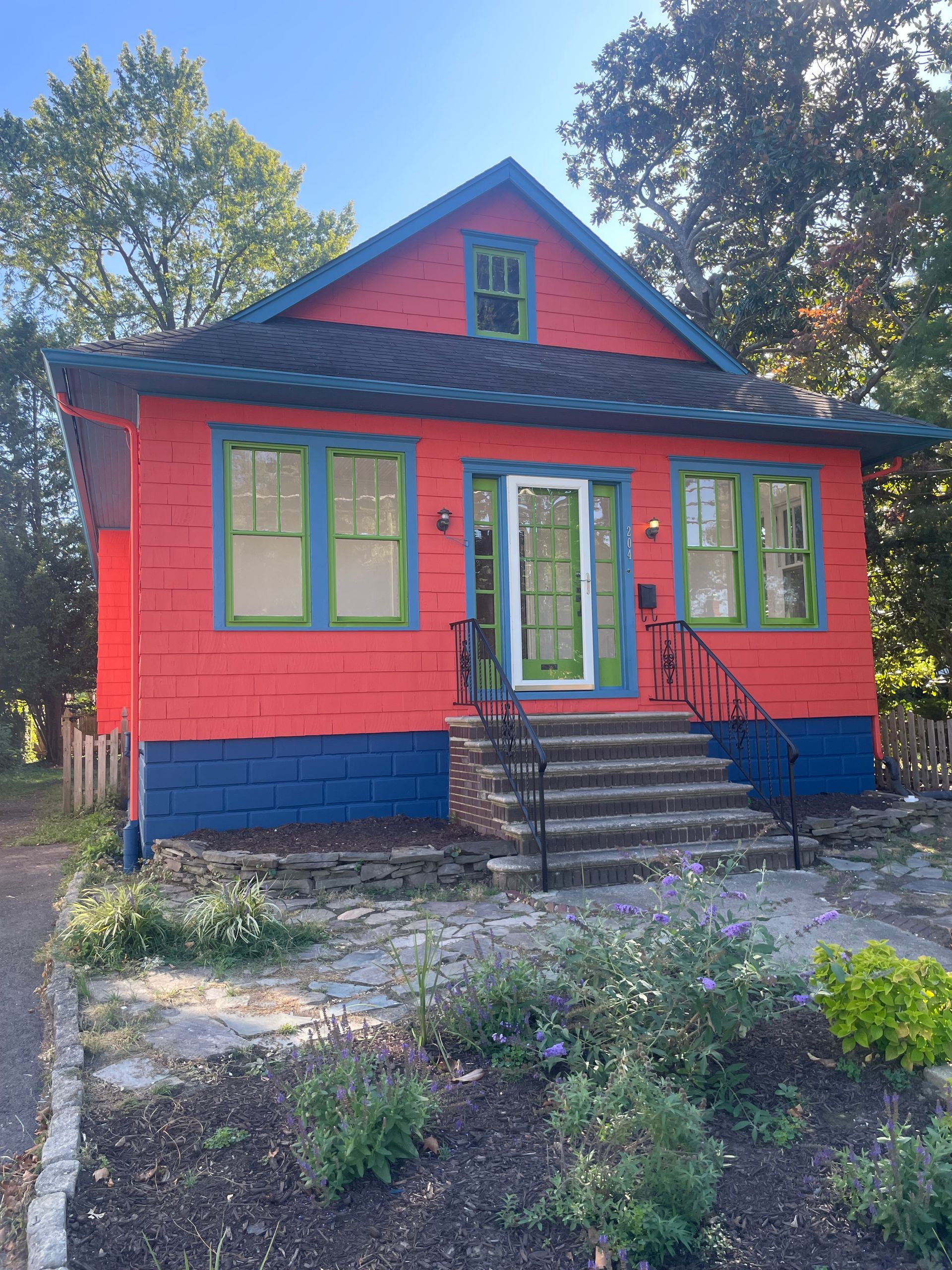 Brightly painted house with red walls, blue trim, and green window frames. Front door has steps leading to it.