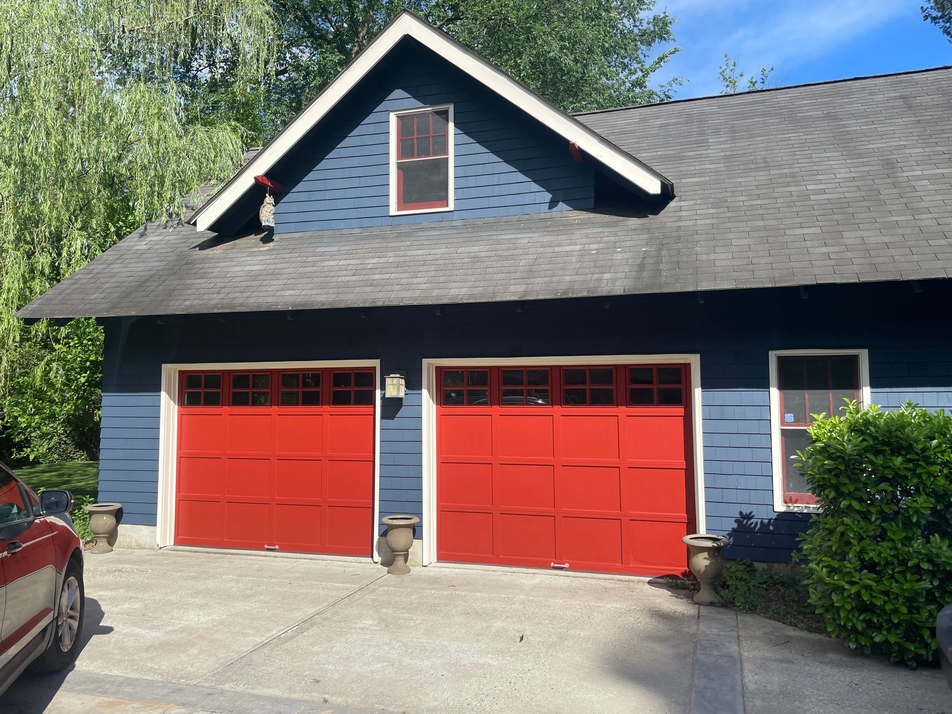 Blue house with red garage doors and a small window under the peak of the roof.