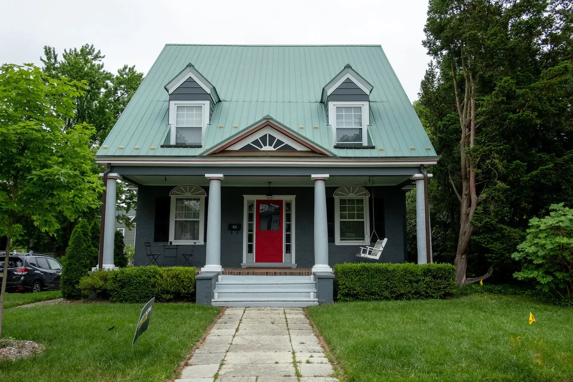 Gray house with green roof, red door, white porch, and swing. Stone walkway leads to the entrance.