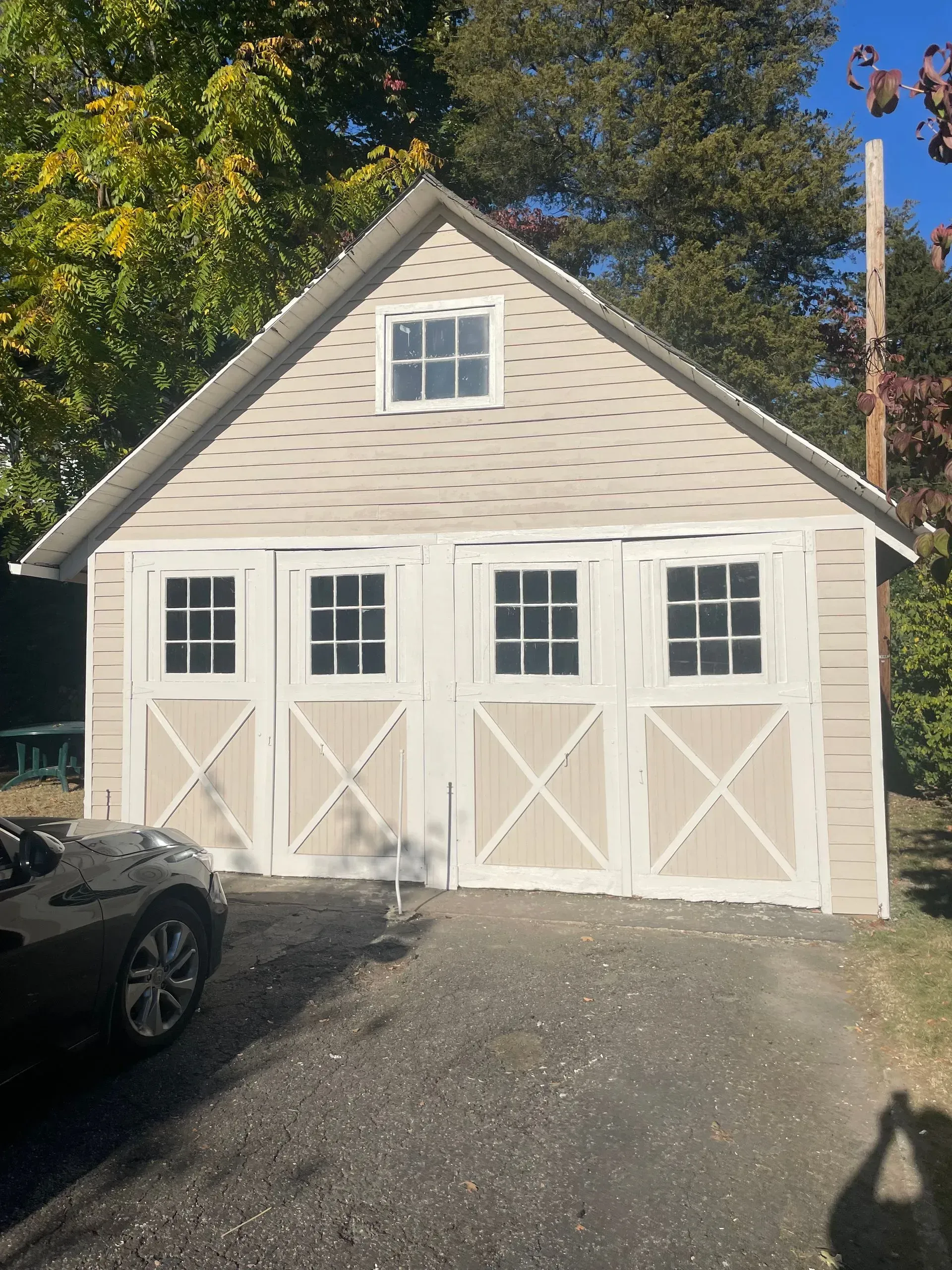 Tan garage with white doors and trim, small square window, asphalt driveway, car parked in front.