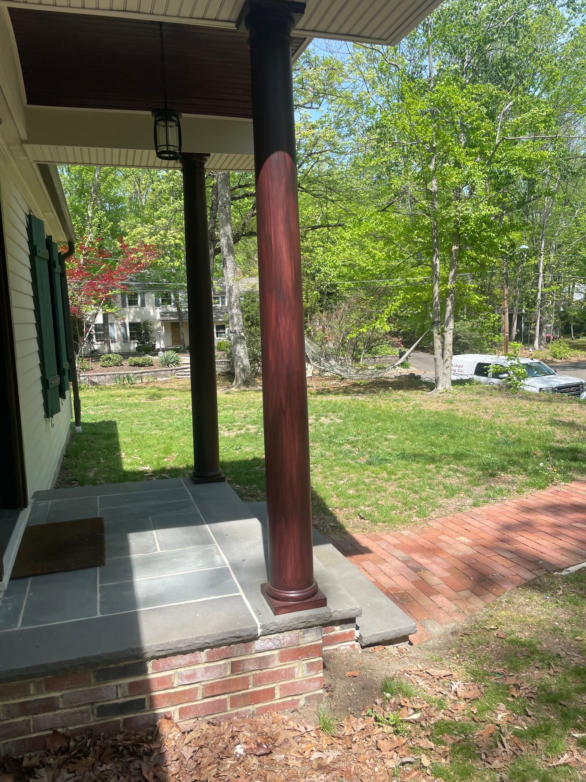 Covered porch with dark wood columns and brick path leading to green yard.