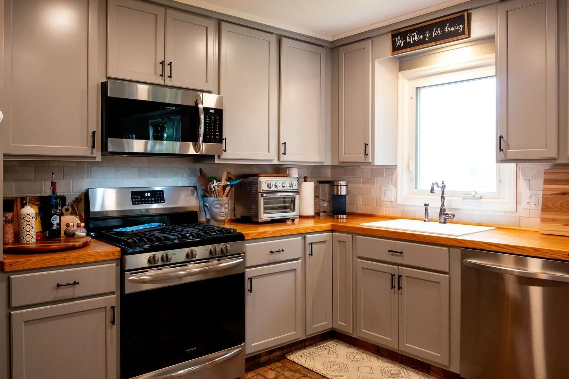 Modern kitchen with stainless steel appliances, light cabinets, and wood countertops under a bright window