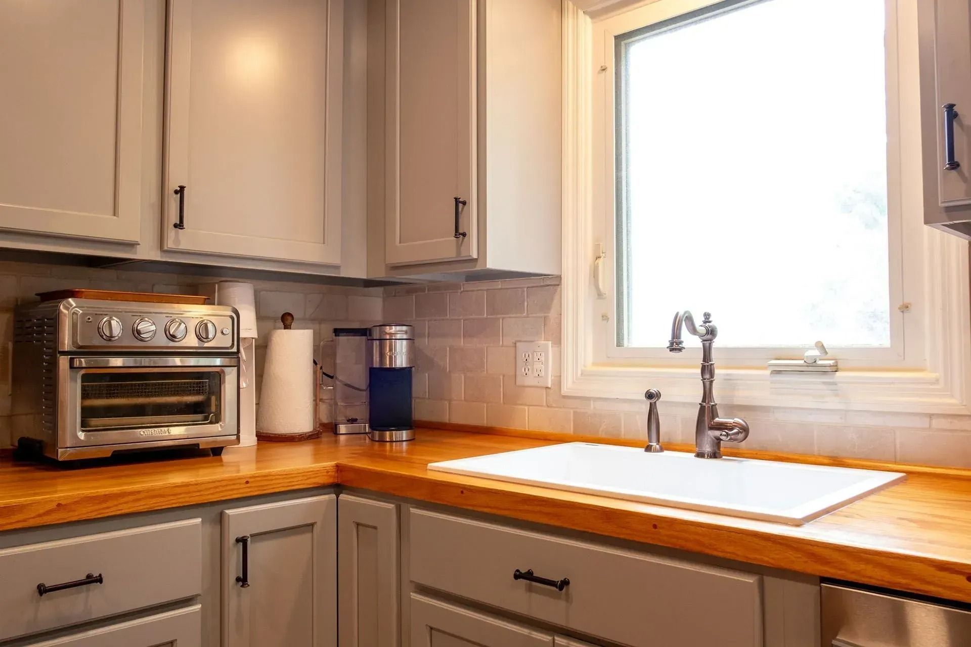 Bright kitchen corner with wooden countertops, gray cabinets, toaster oven, and sink by a sunny window