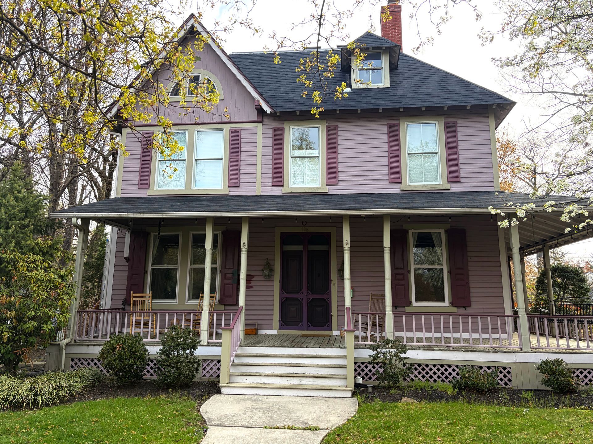 Victorian-style house with purple siding, white trim, and a front porch behind bare trees