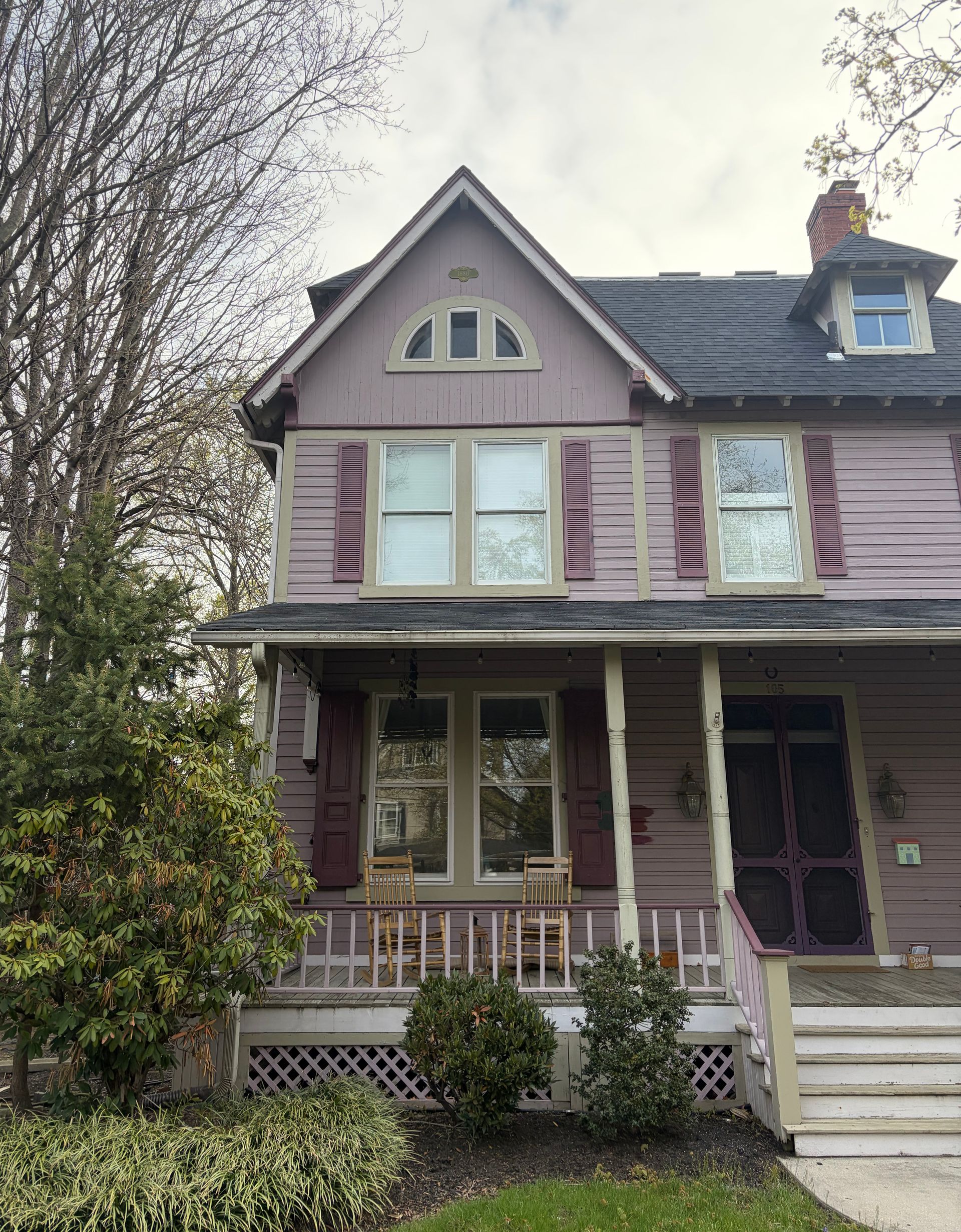 Victorian-style pink house with purple shutters and a front porch, viewed from the street