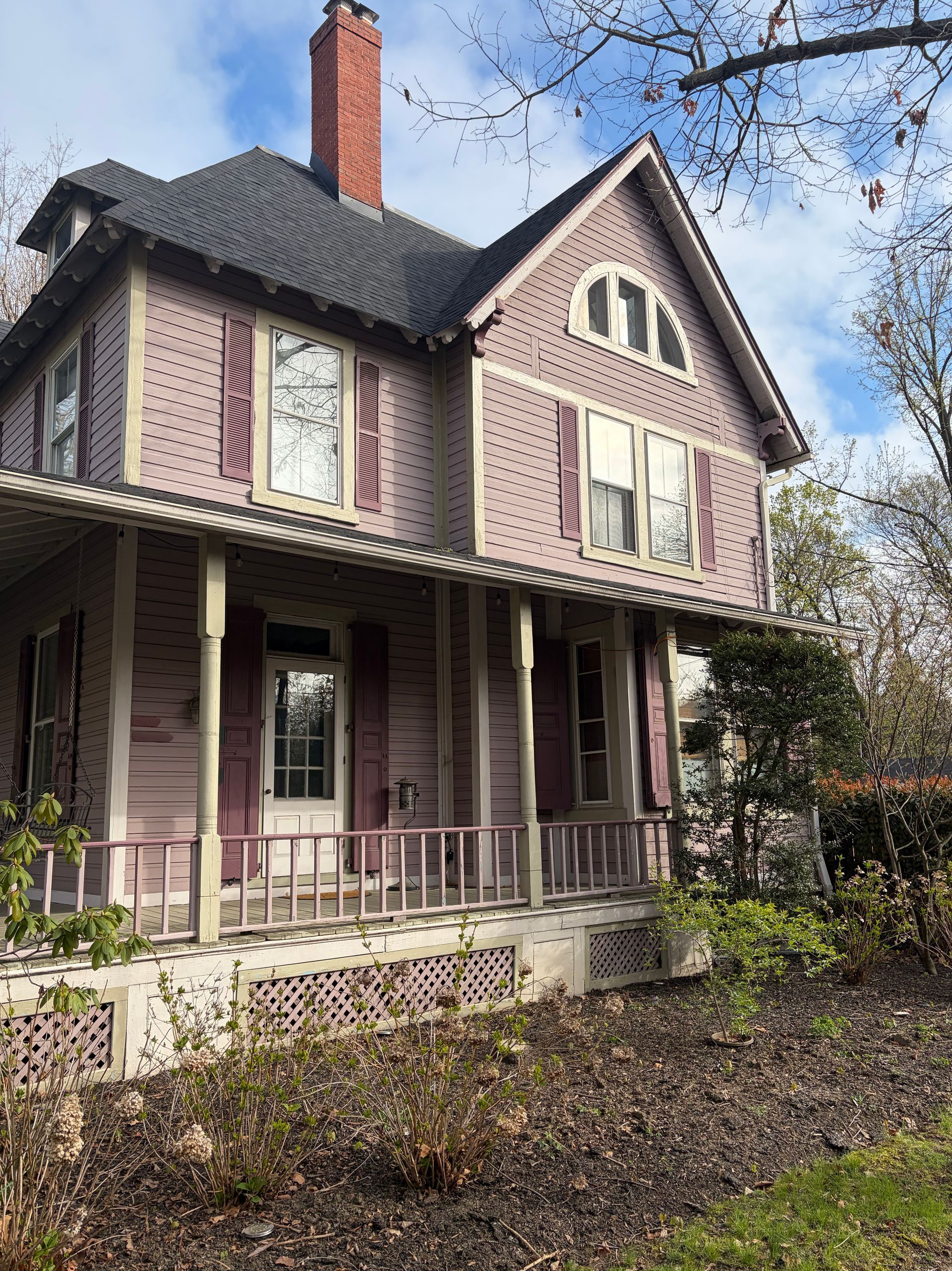 Victorian house with pink siding, steep gabled roof, and a front porch surrounded by autumn trees.