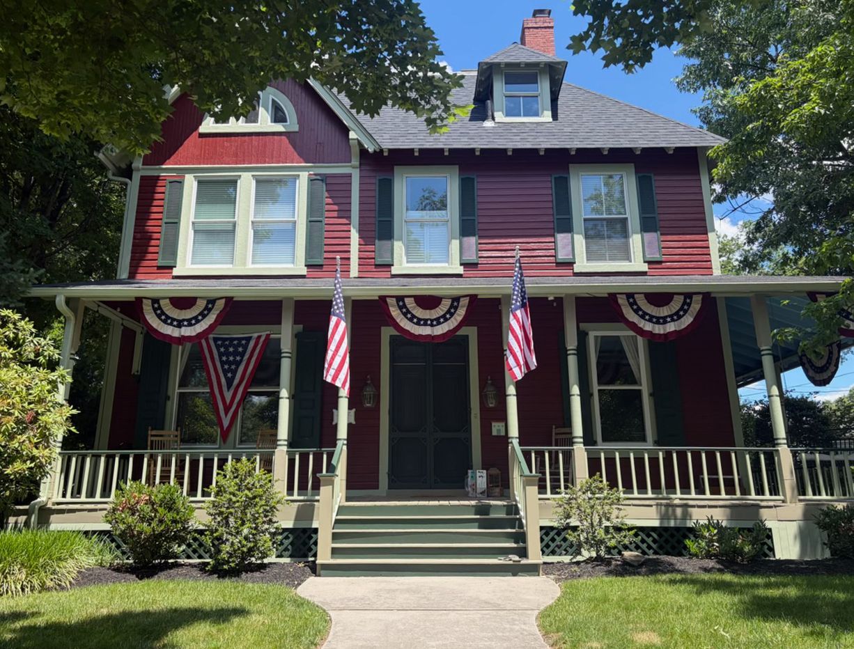 Victorian house with red trim, American flags, and patriotic bunting on the front porch
