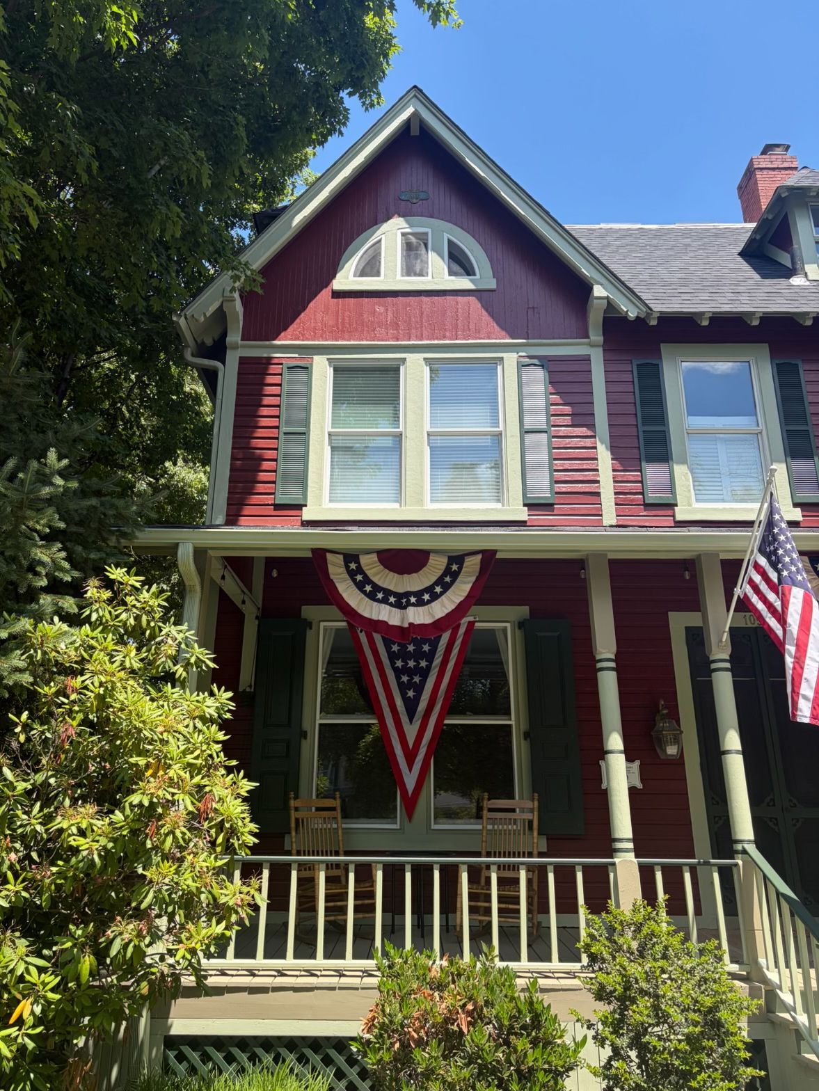 Victorian house with burgundy siding, white trim, front porch, and patriotic bunting and flags.