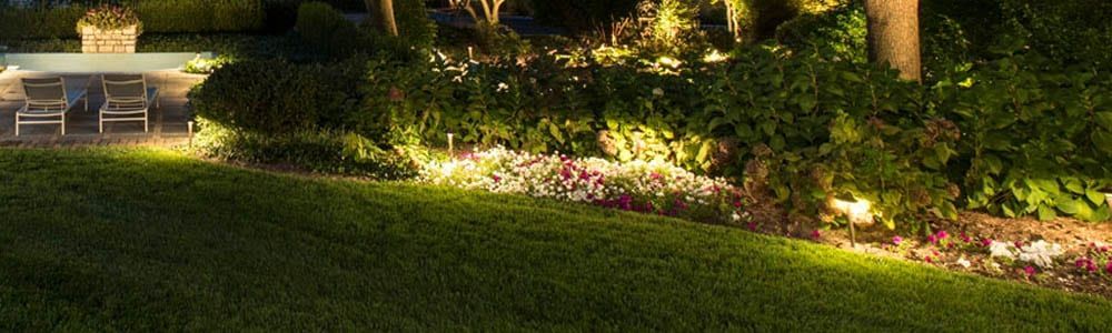 Dimly lit garden path with flower beds and a stone bench at dusk