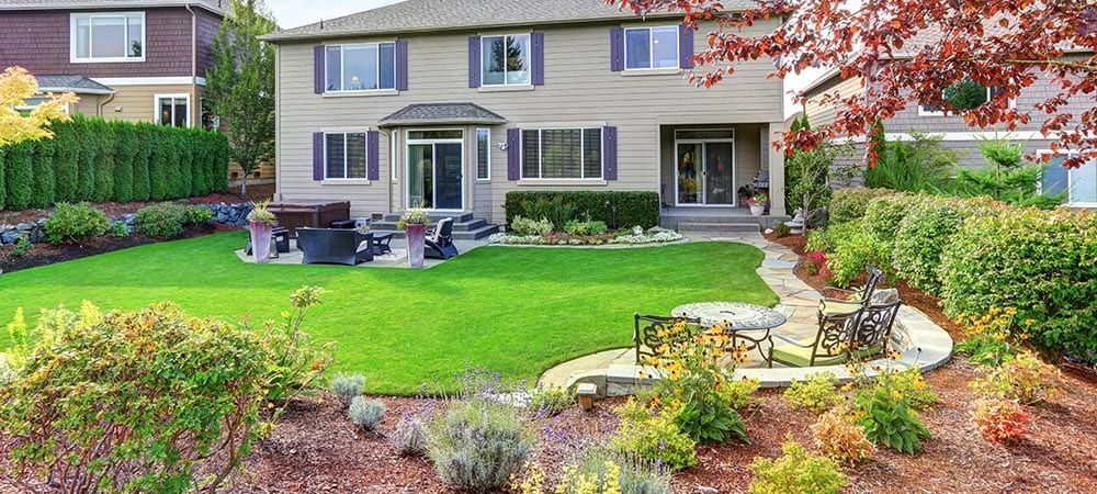 Backyard patio with green lawn, stone seating area, and two-story townhouse in the background