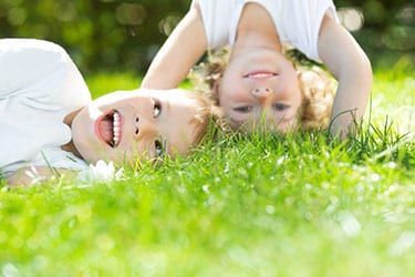 Two children lying in bright green grass, smiling and looking at the camera