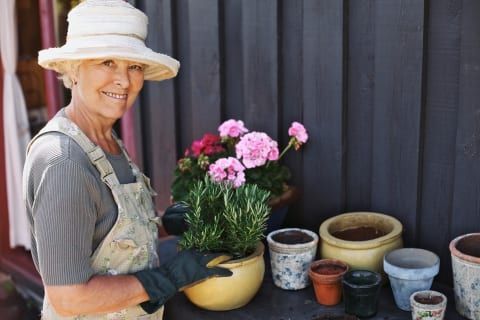Woman in a straw hat holding a potted pink flower beside assorted pots outdoors