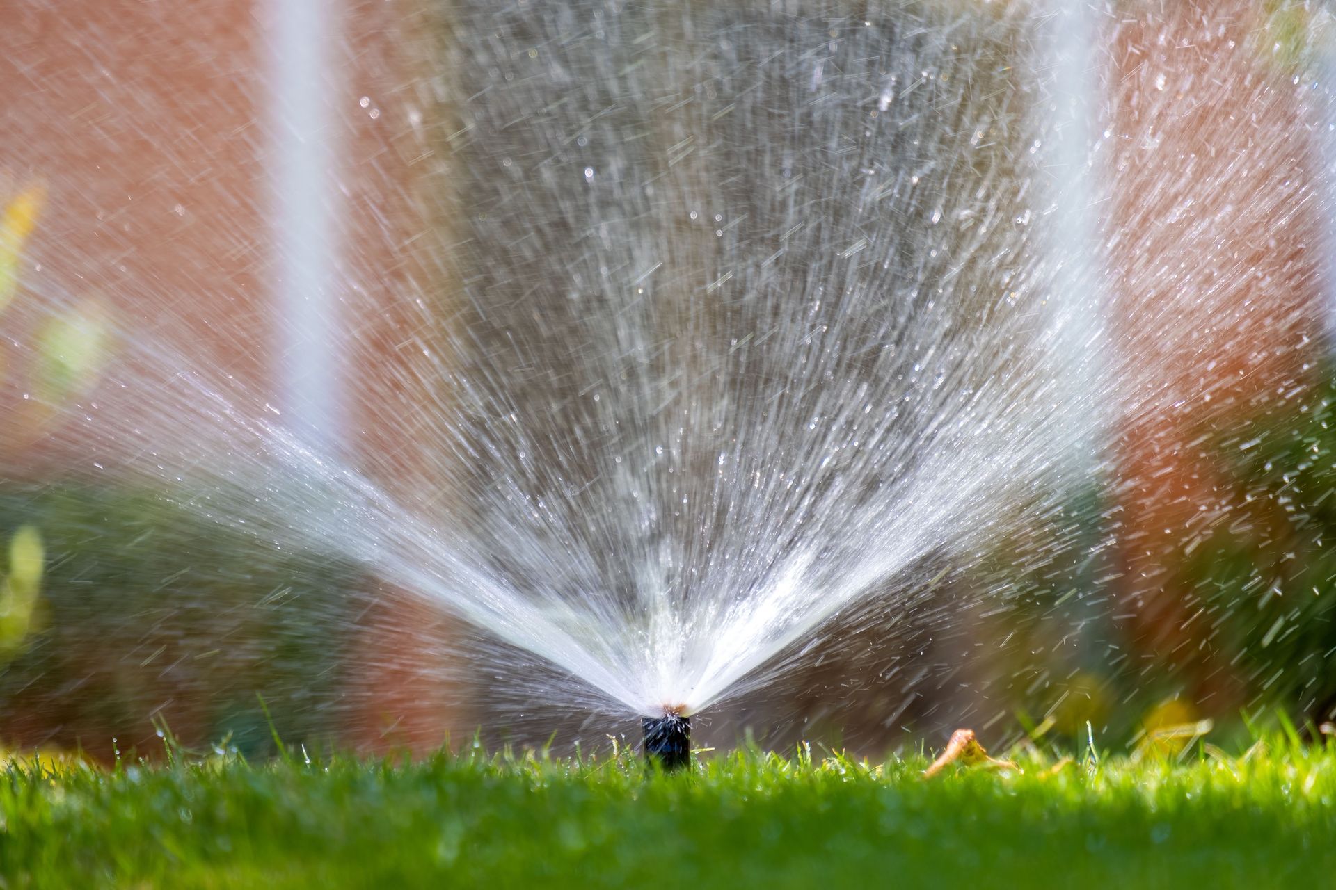 Sprinkler spraying water across a green lawn in front of a brick wall