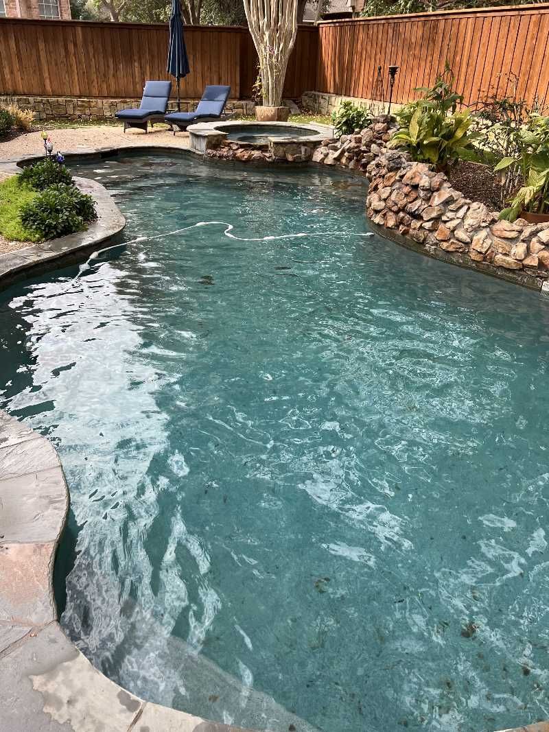 A large swimming pool surrounded by rocks and chairs in a backyard.